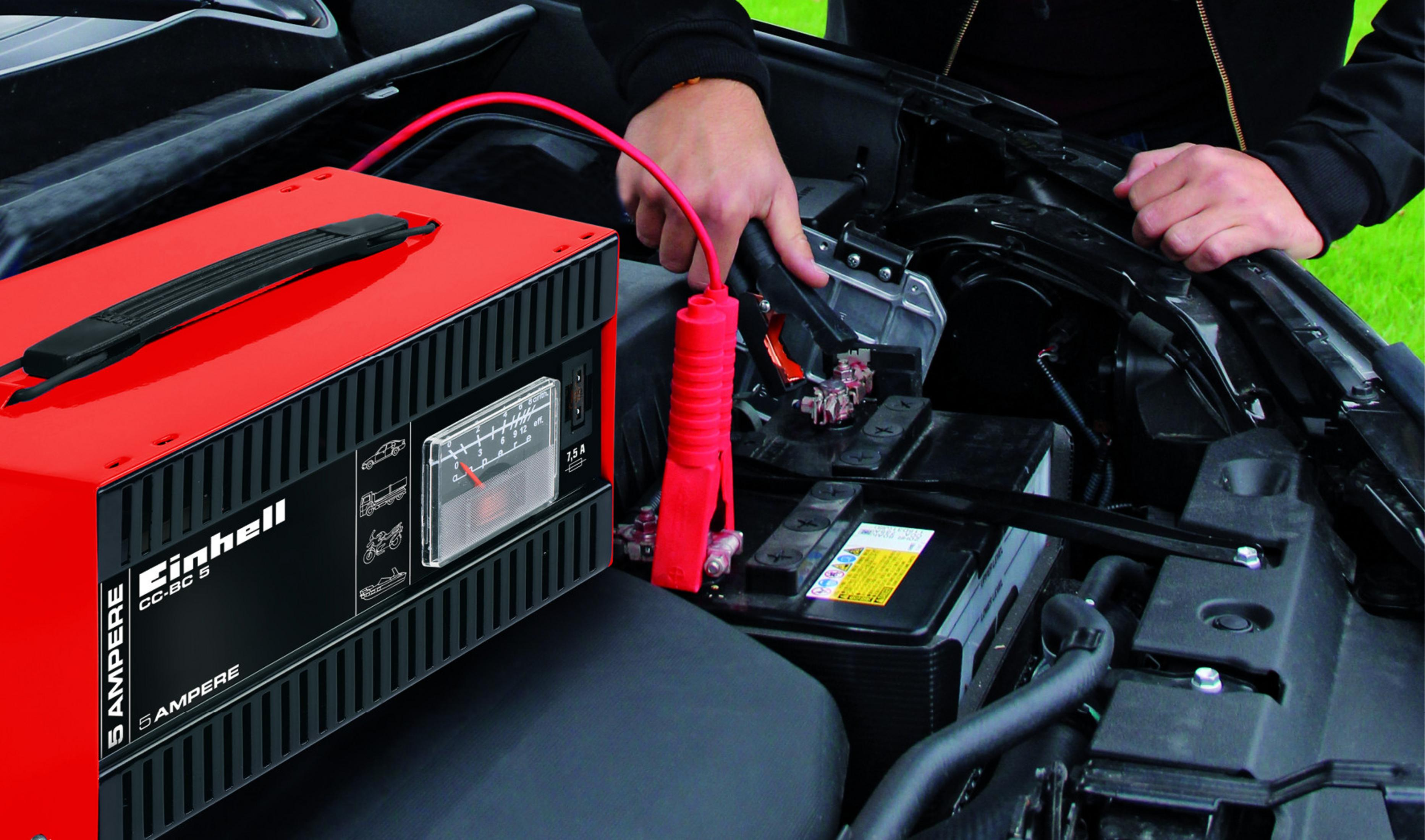 Eine Person schließt ein rotes Autobatterieladegerät an eine Autobatterie an.