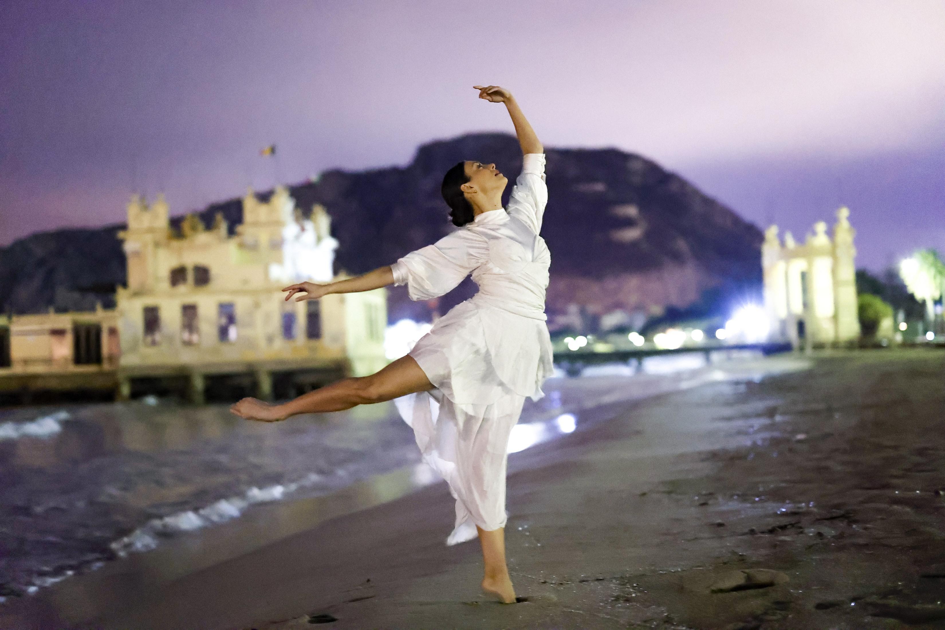Bailarina con vestido blanco baila en la playa por la noche.
