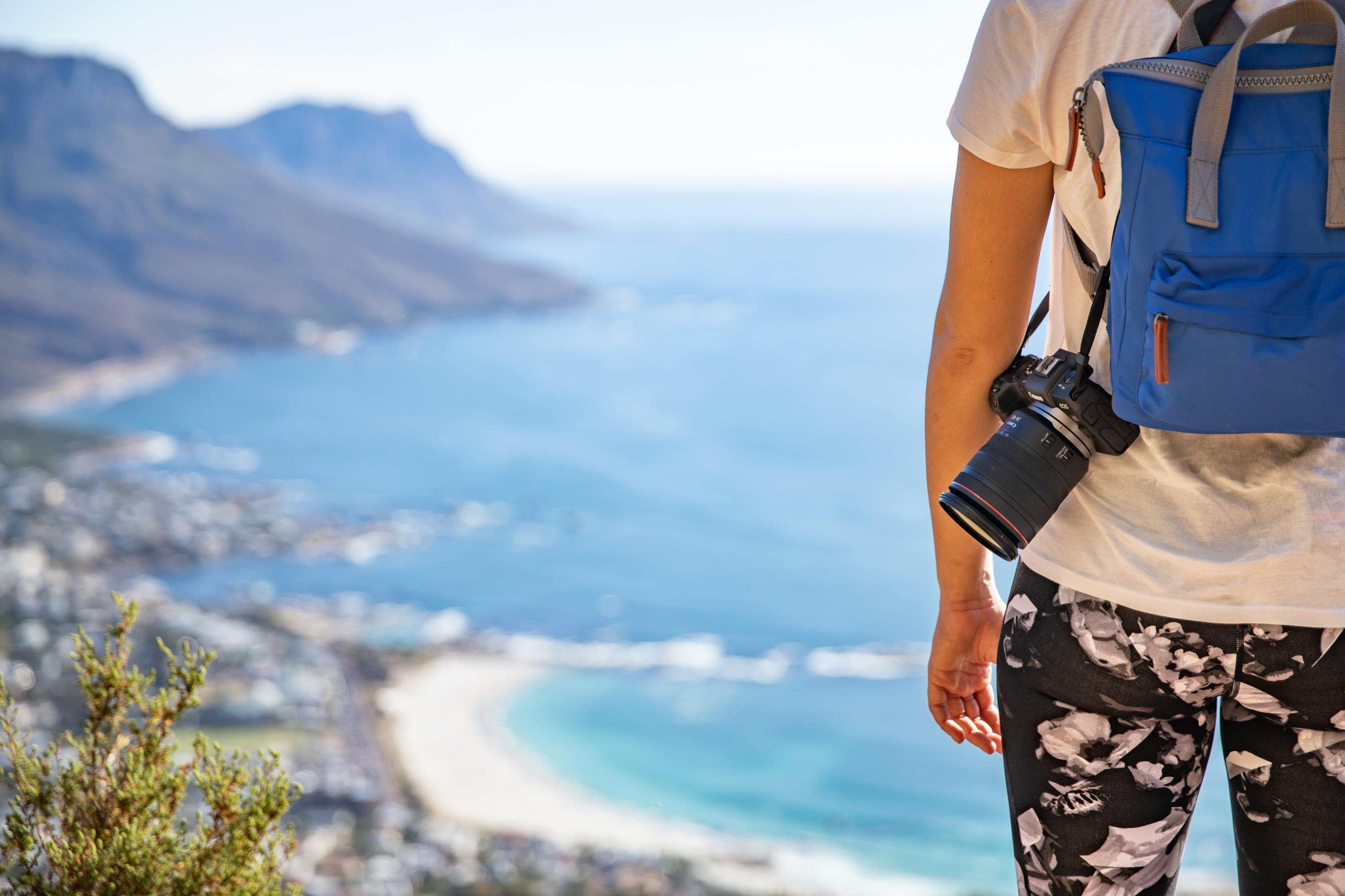 Person mit blauem Rucksack und Kamera, Blick auf Küstenlandschaft.