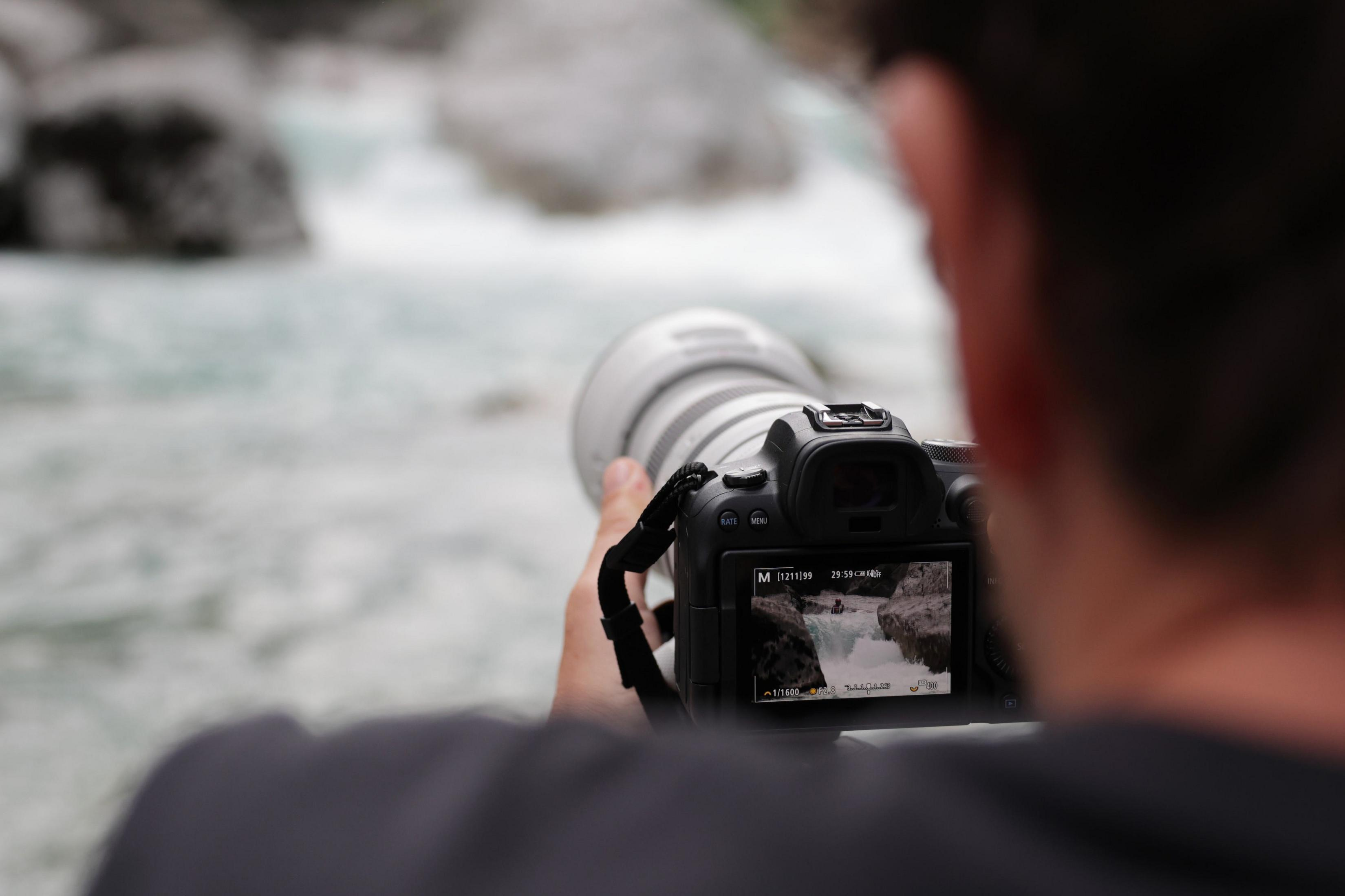 Persona sosteniendo una cámara, tomando una foto de un río de flujo rápido.