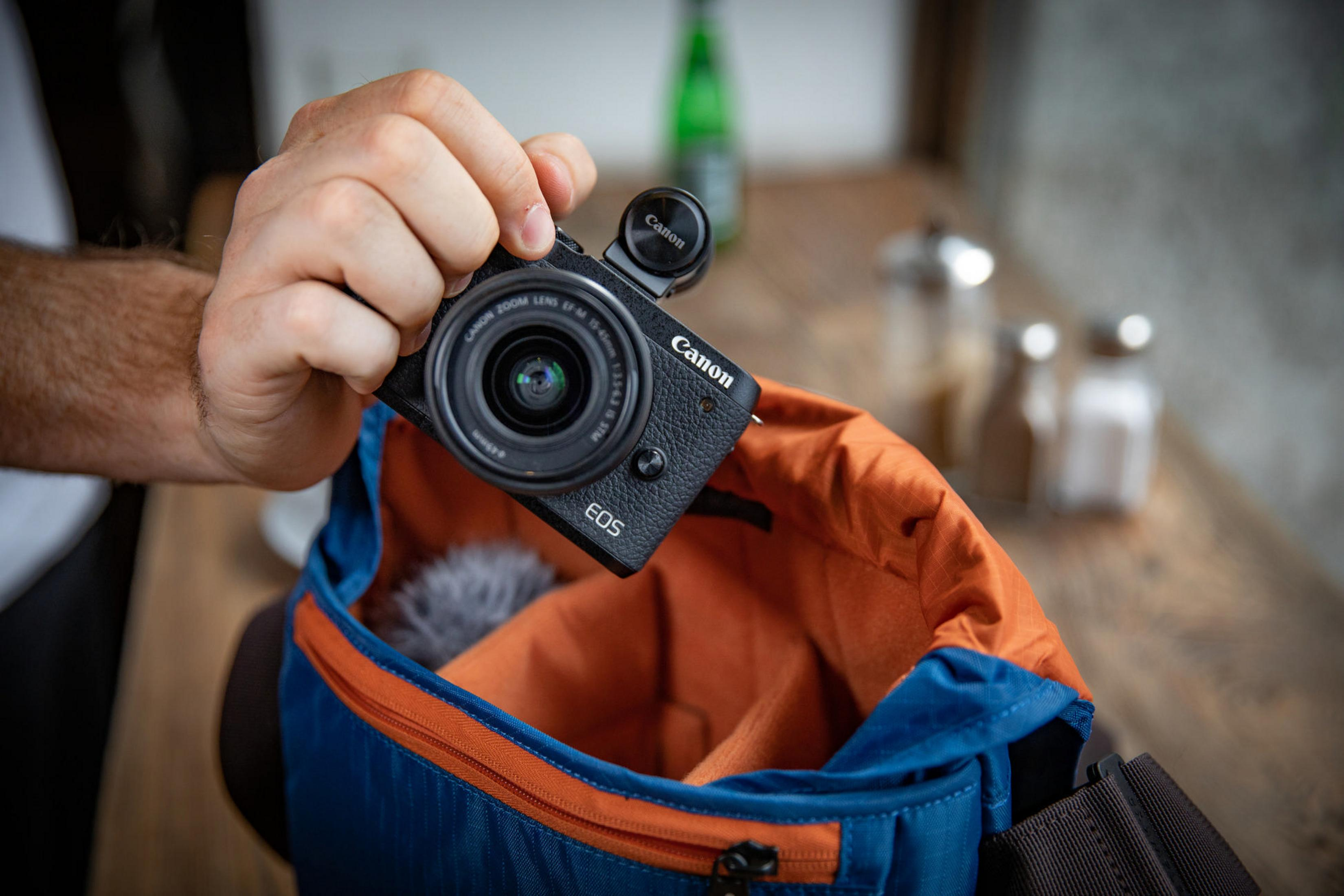 Person hält Canon Kamera und legt sie in eine Tasche.