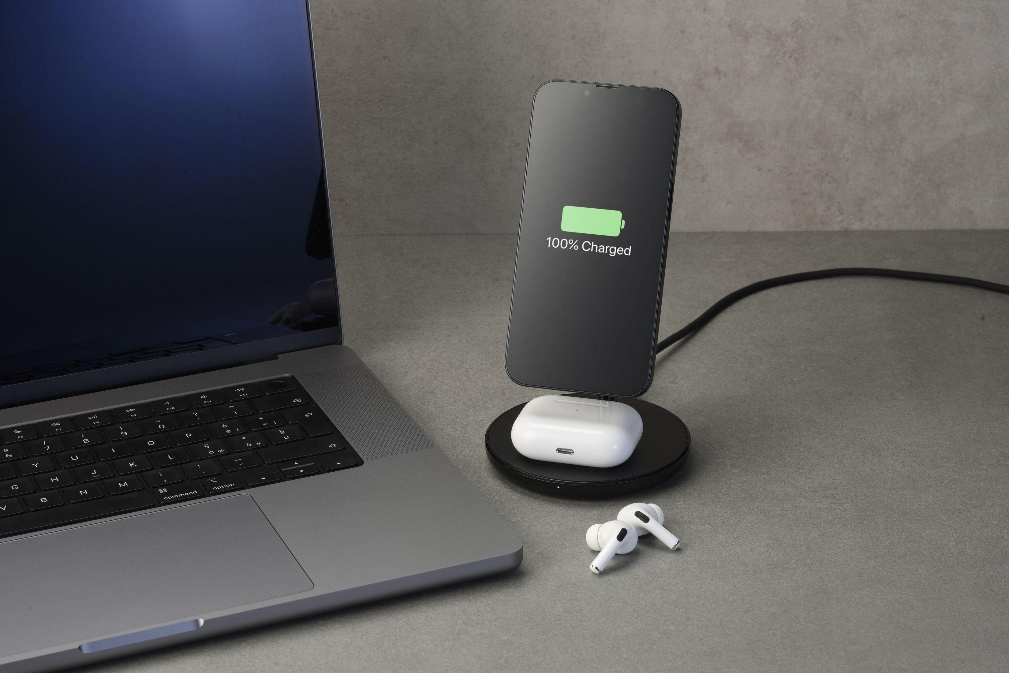 Laptop und Telefon auf einem Schreibtisch. Das Telefon wird kabellos aufgeladen. AirPods daneben.
