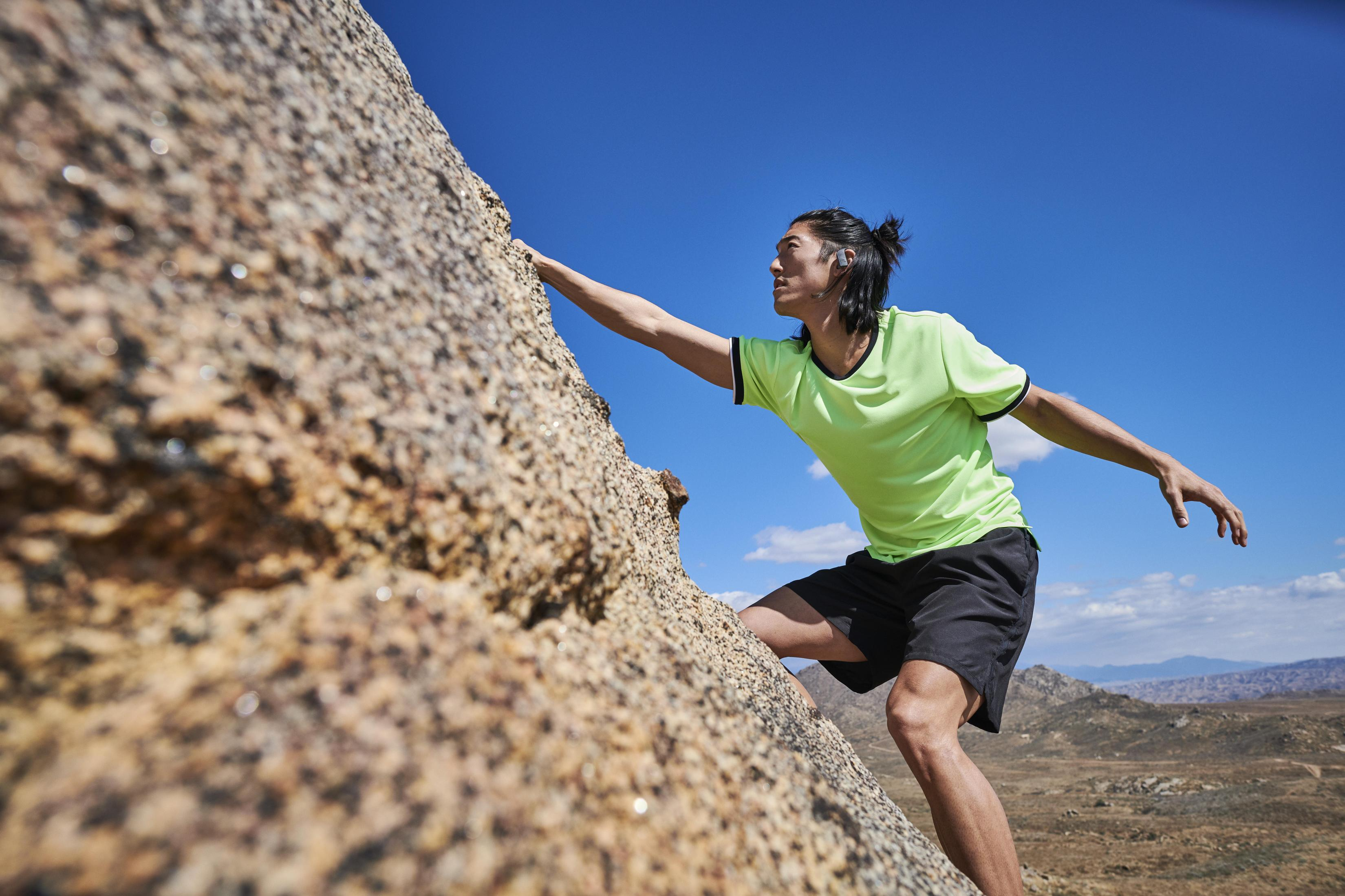 Mężczyzna wspinający się po skale, wyciągający rękę. Błękitne niebo i krajobraz pustynny.