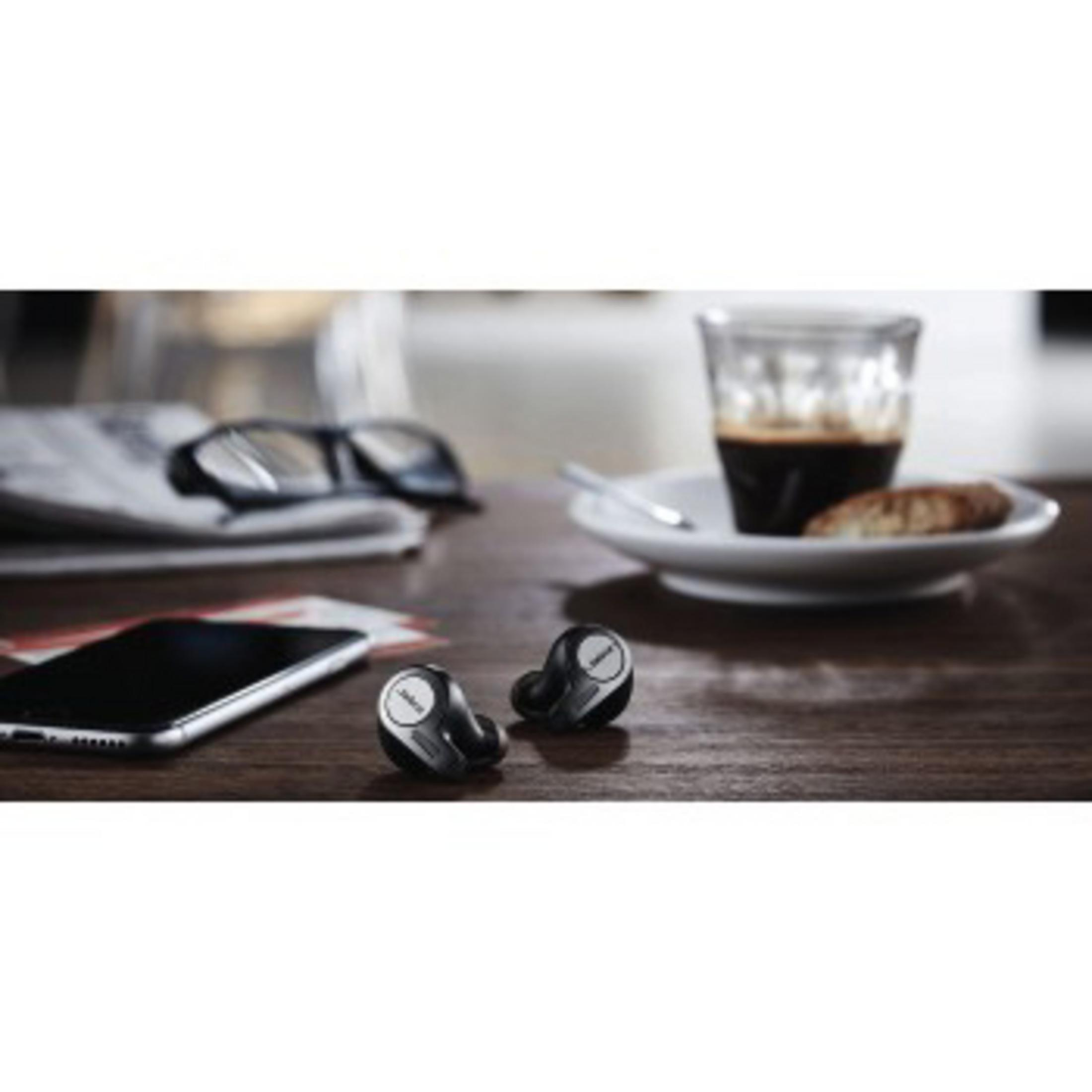 Auricolari, un telefono, occhiali, caffè e un pasticcino sono su un tavolo di legno. Lo sfondo è sfocato.