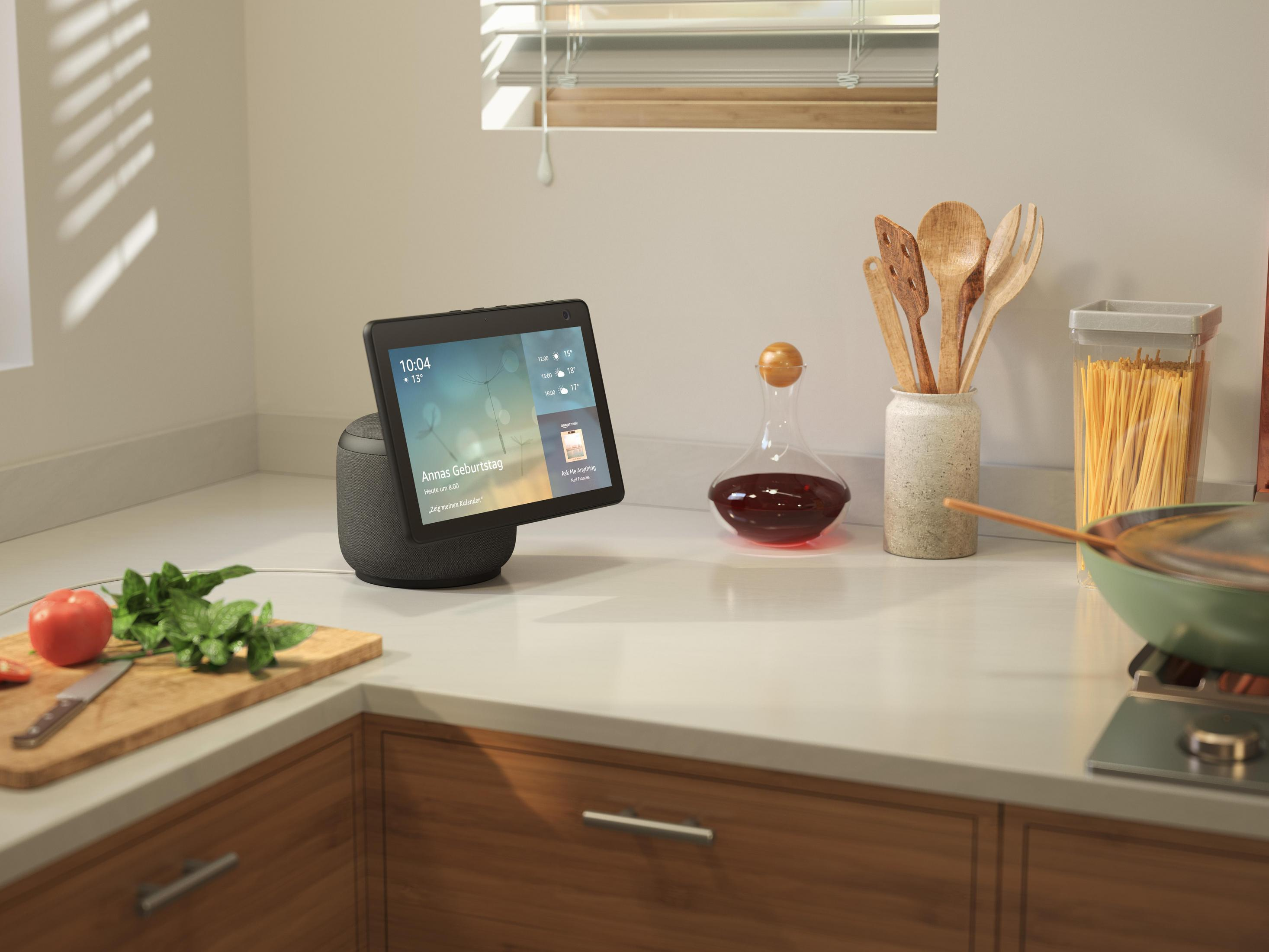 Smart Home Gerät mit Bildschirm auf Küchenarbeitsplatte mit Küchenutensilien.