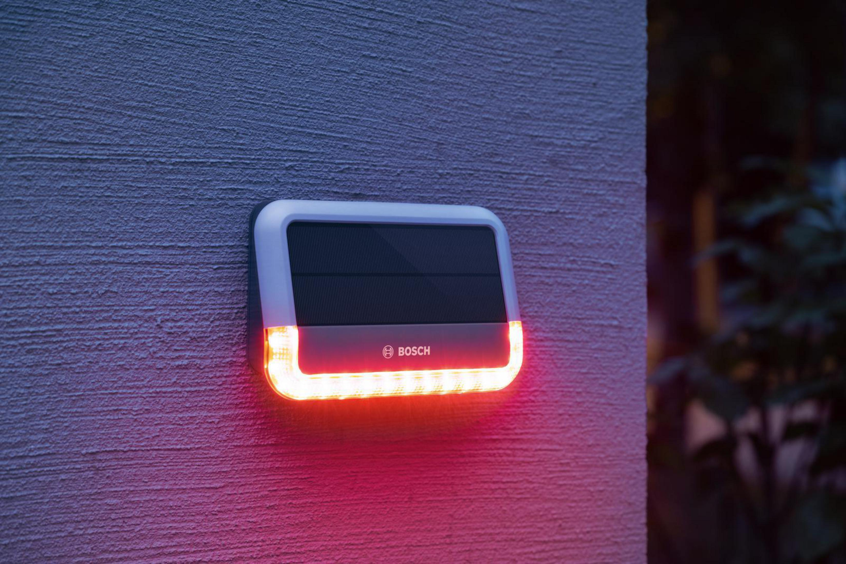 Ein dunkelgrauer, an der Wand montierter Bosch-Alarm. Es hat rote leuchtende Lichter.