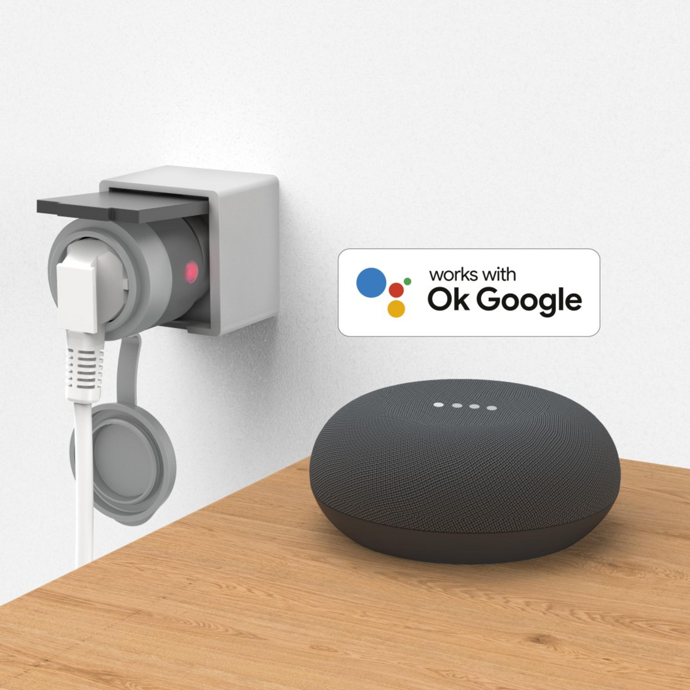 Ein schwarzer Google Nest Mini Lautsprecher auf einem Holztisch neben einer Steckdose mit eingestecktem Gerät.