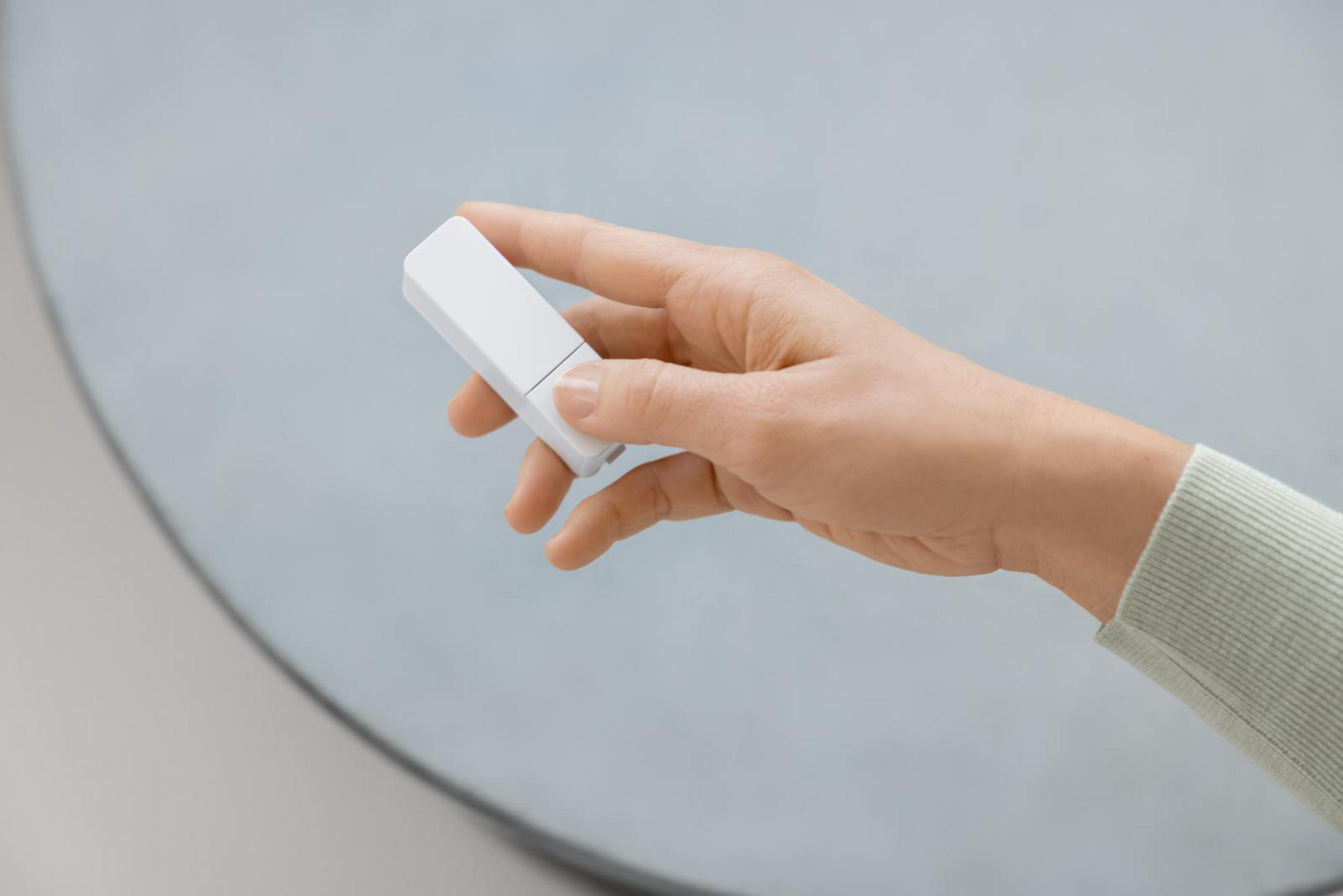 Dłoń trzymająca białą, prostokątną pamięć USB.