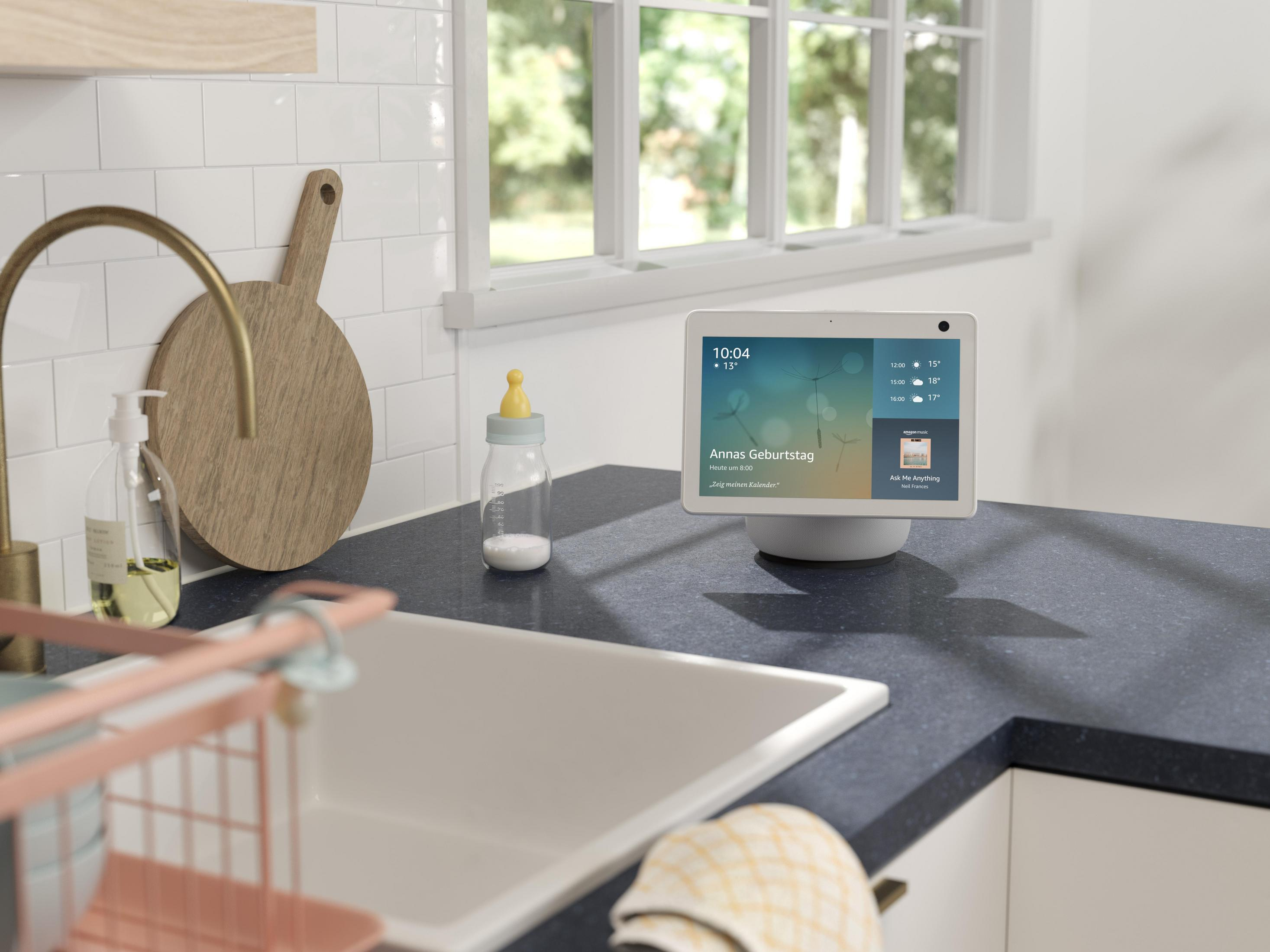 Smart-Home-Gerät auf einer Theke in einer Küche, zeigt Kalender- und Wetterinformationen.
