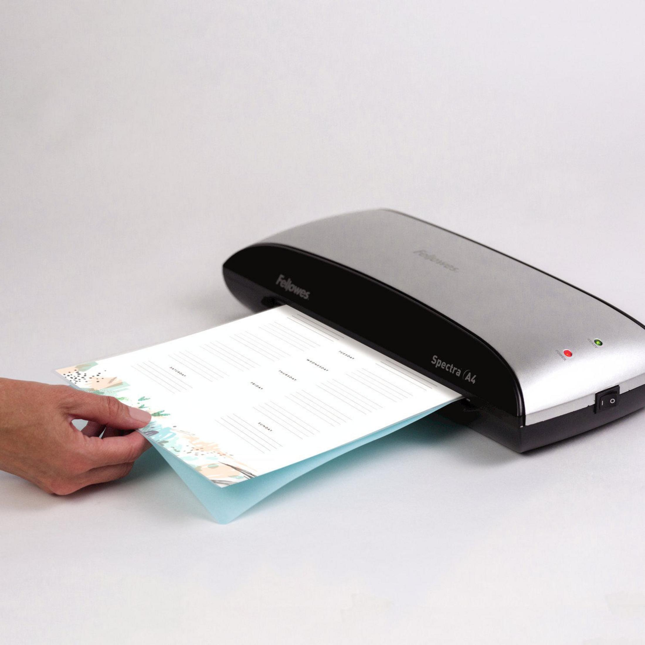 Ręka wkładająca kartkę papieru do laminatora, z kalendarzem kwiatowym na papierze.