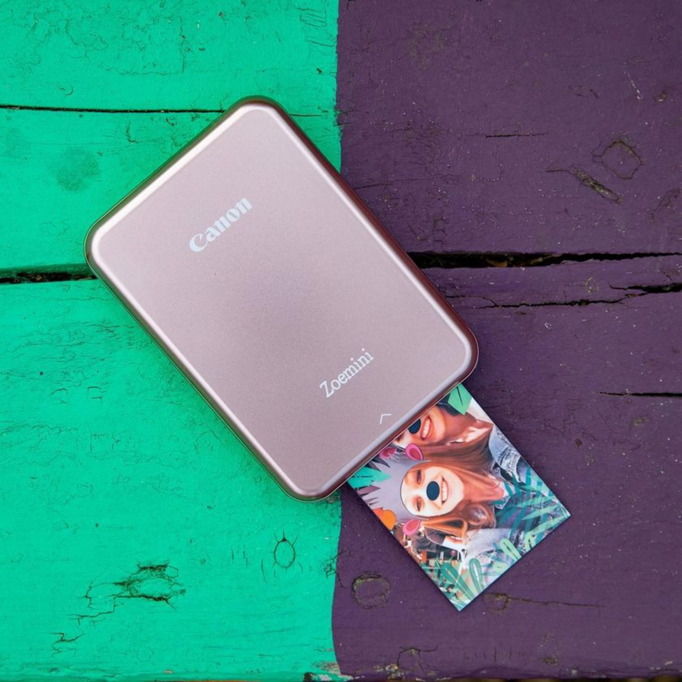 Różowa drukarka Canon Zoemini na zielono-fioletowej powierzchni ze zdjęciem.