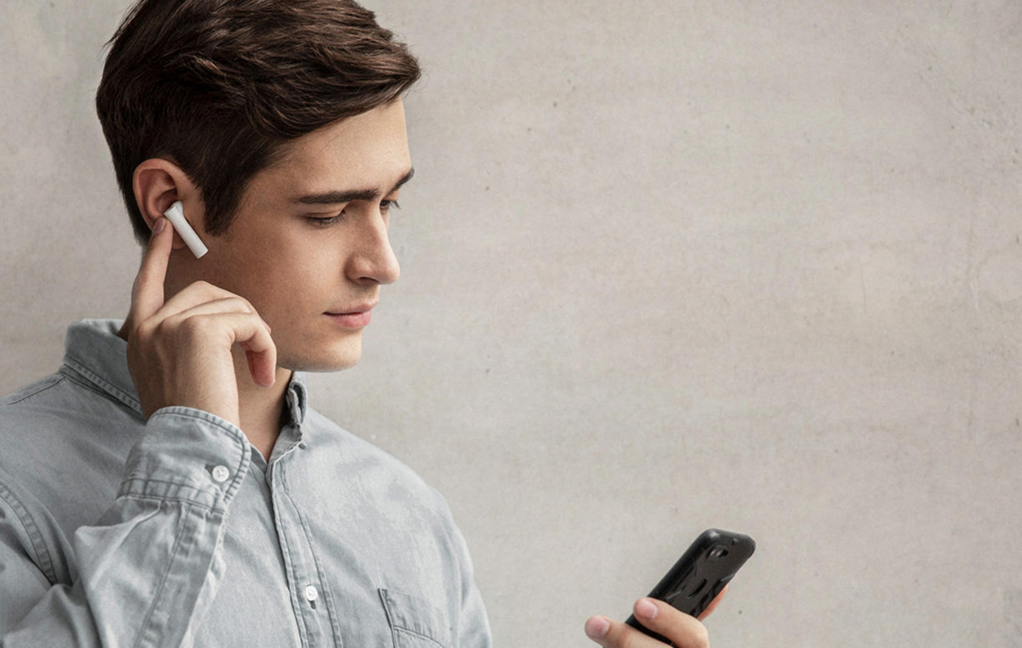 Mężczyzna ze słuchawką w uchu, patrzący na telefon w dłoni.