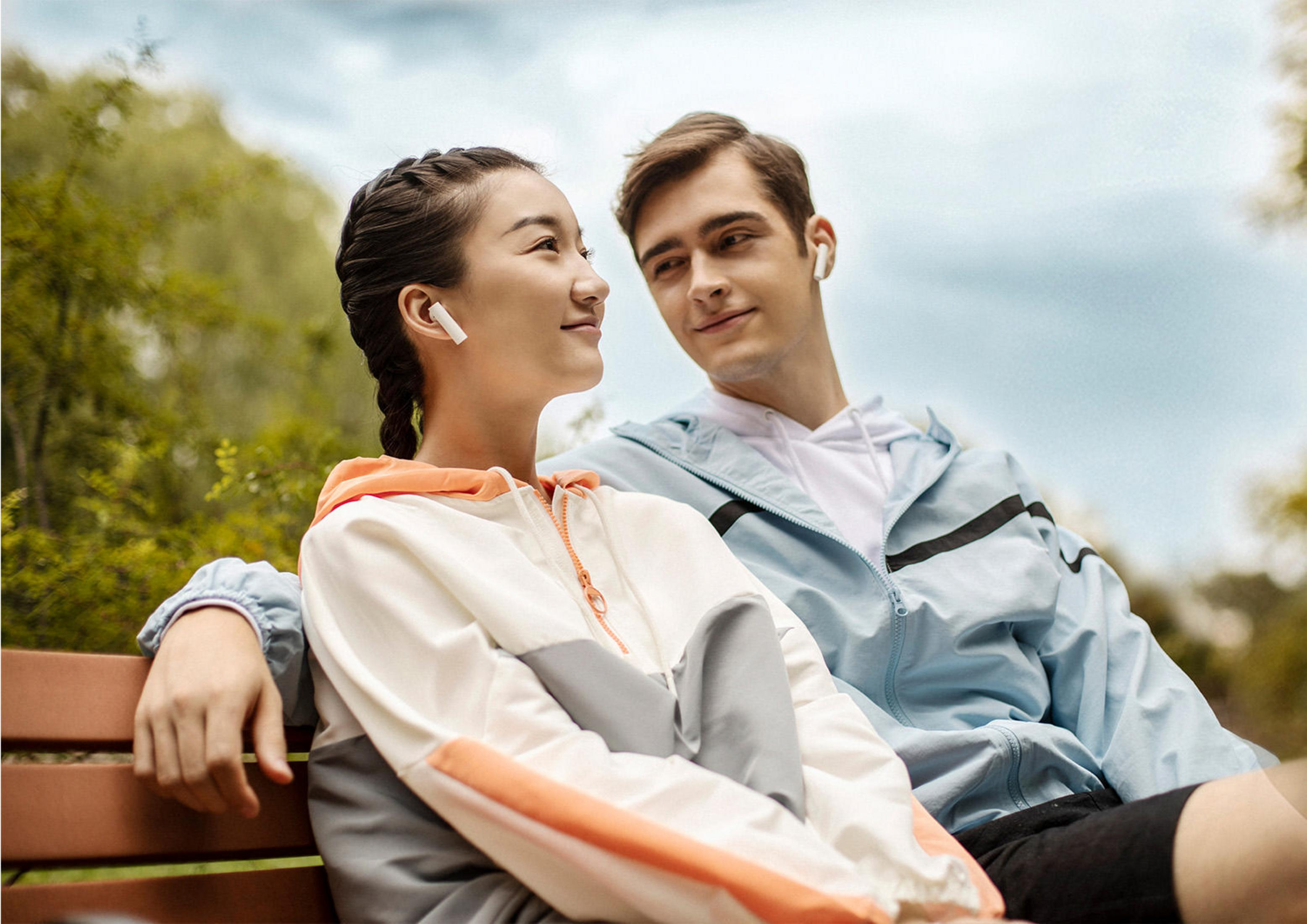 Para siedząca na ławce, oboje w słuchawkach. Patrzą na siebie w parku.