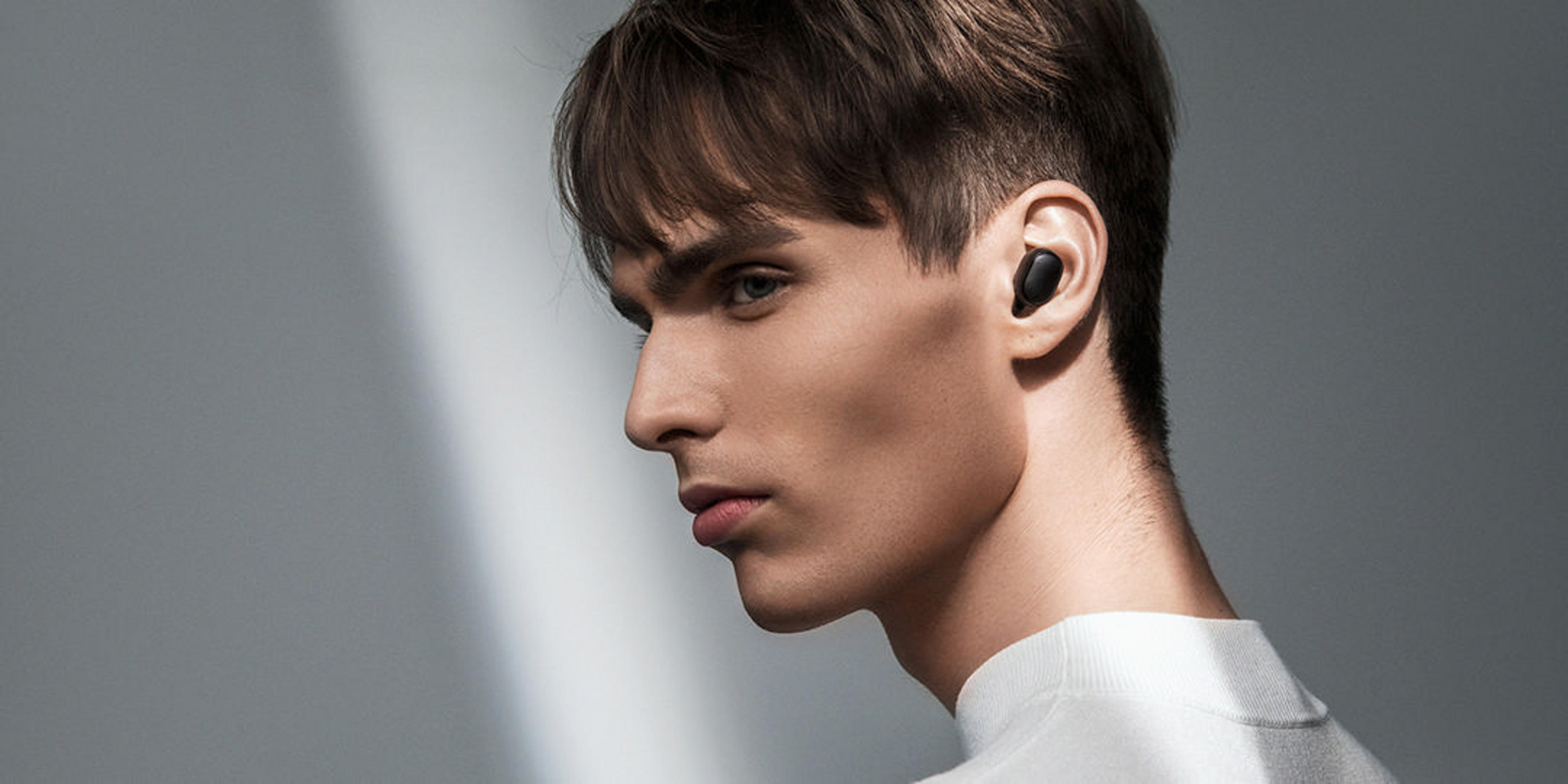 Un hombre con un auricular en una oreja, mirando hacia la izquierda, sobre un fondo degradado.