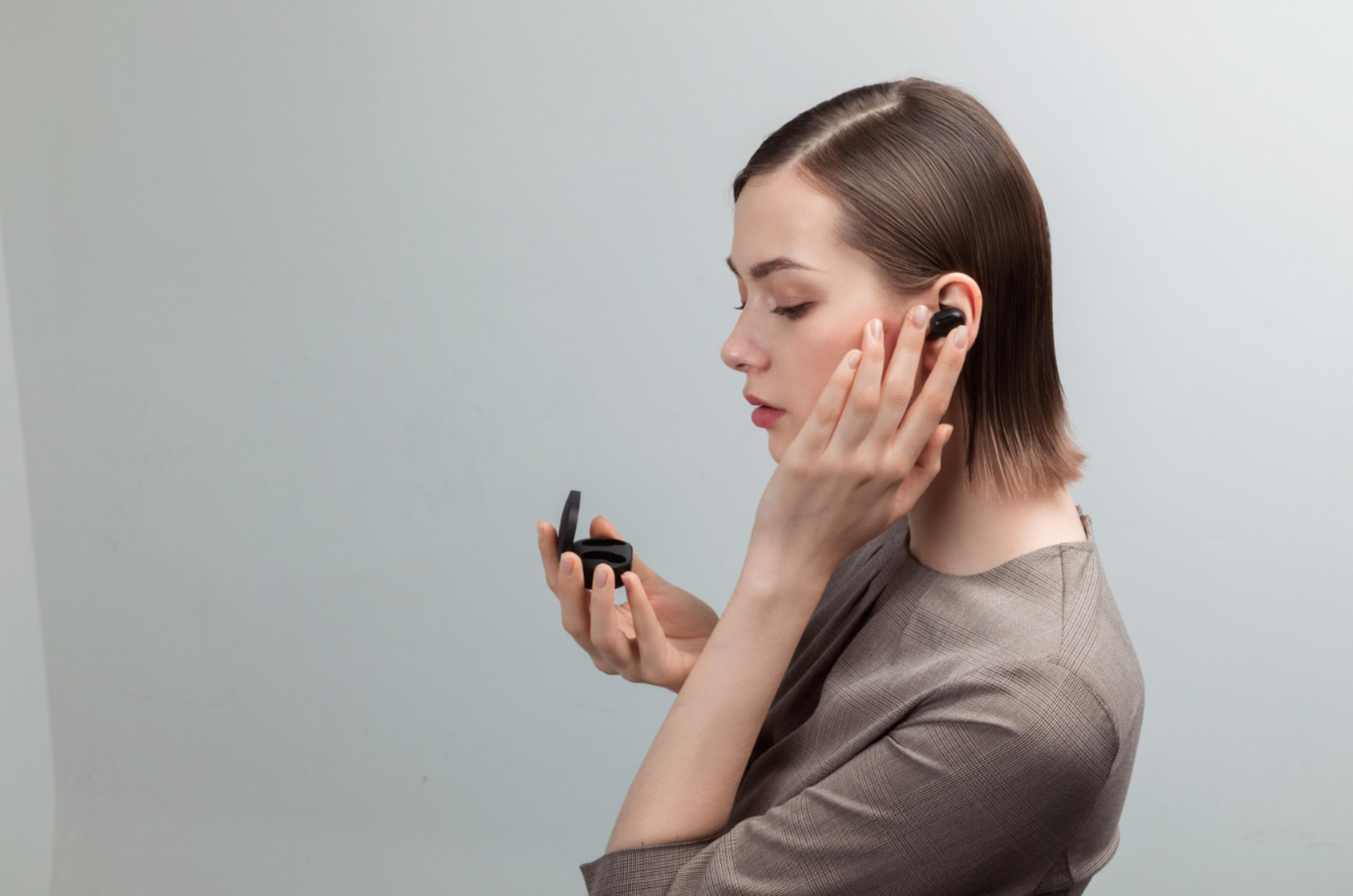 Una mujer poniéndose un auricular en la oreja, sosteniendo el estuche en la mano.
