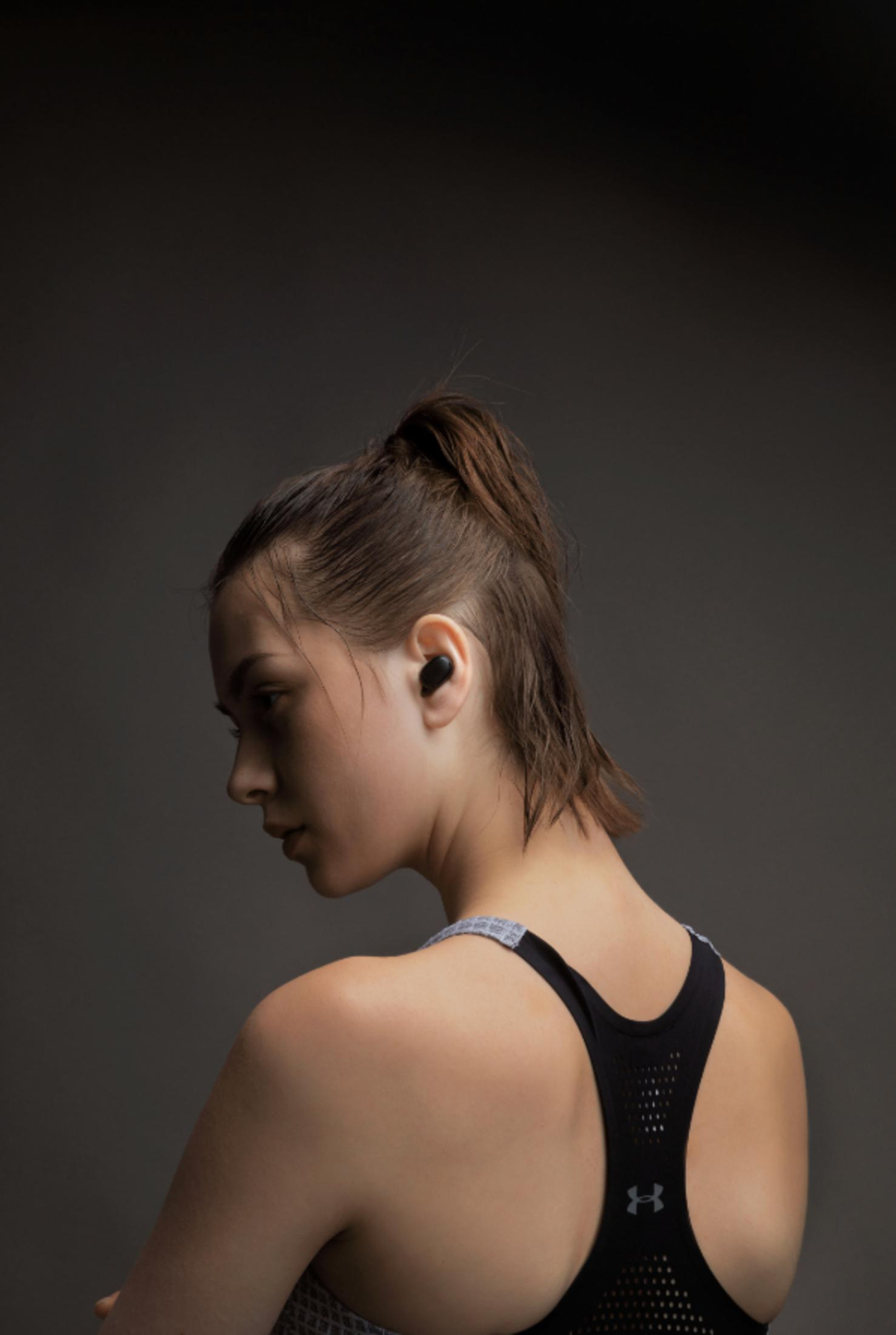 Mujer con un auricular, mirando a la izquierda, fondo oscuro. Con sujetador deportivo.