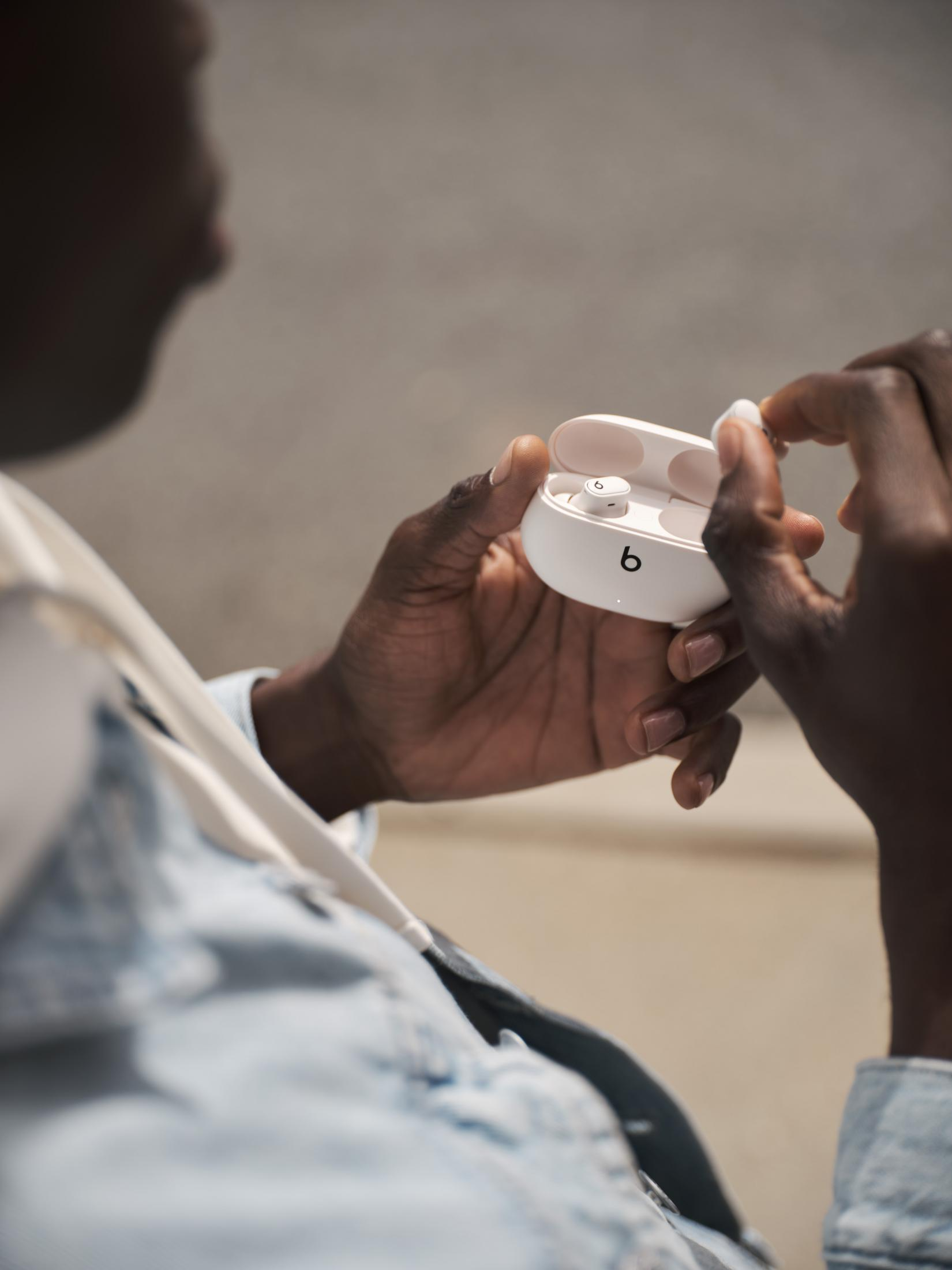 Osoba trzymająca białe etui na słuchawki Beats, z otwartym etui ujawniającym słuchawki w środku.