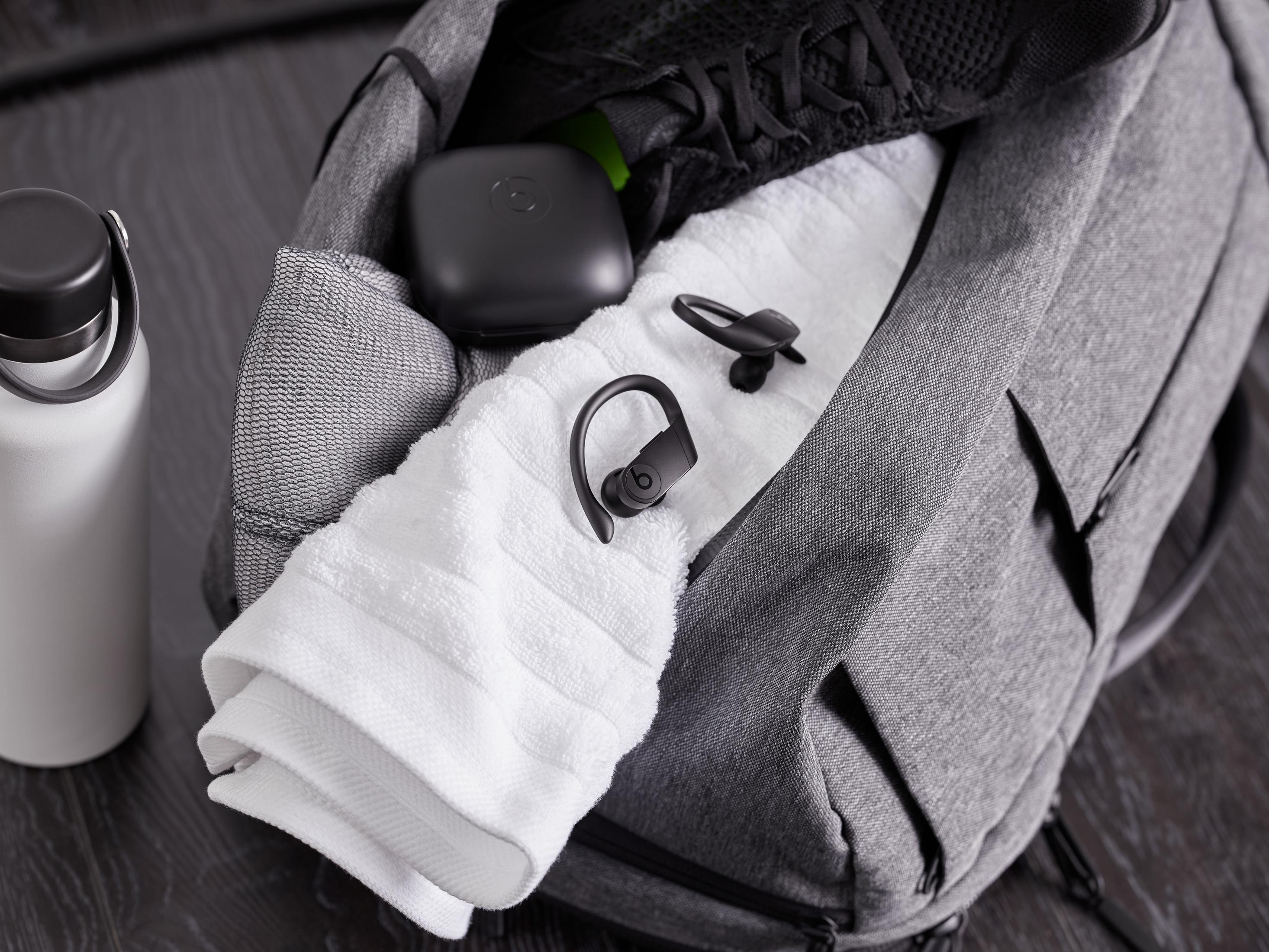 Szara torba sportowa ze słuchawkami, ręcznikiem, butelką wody i czarnym etui w środku. Słuchawki są czarne.