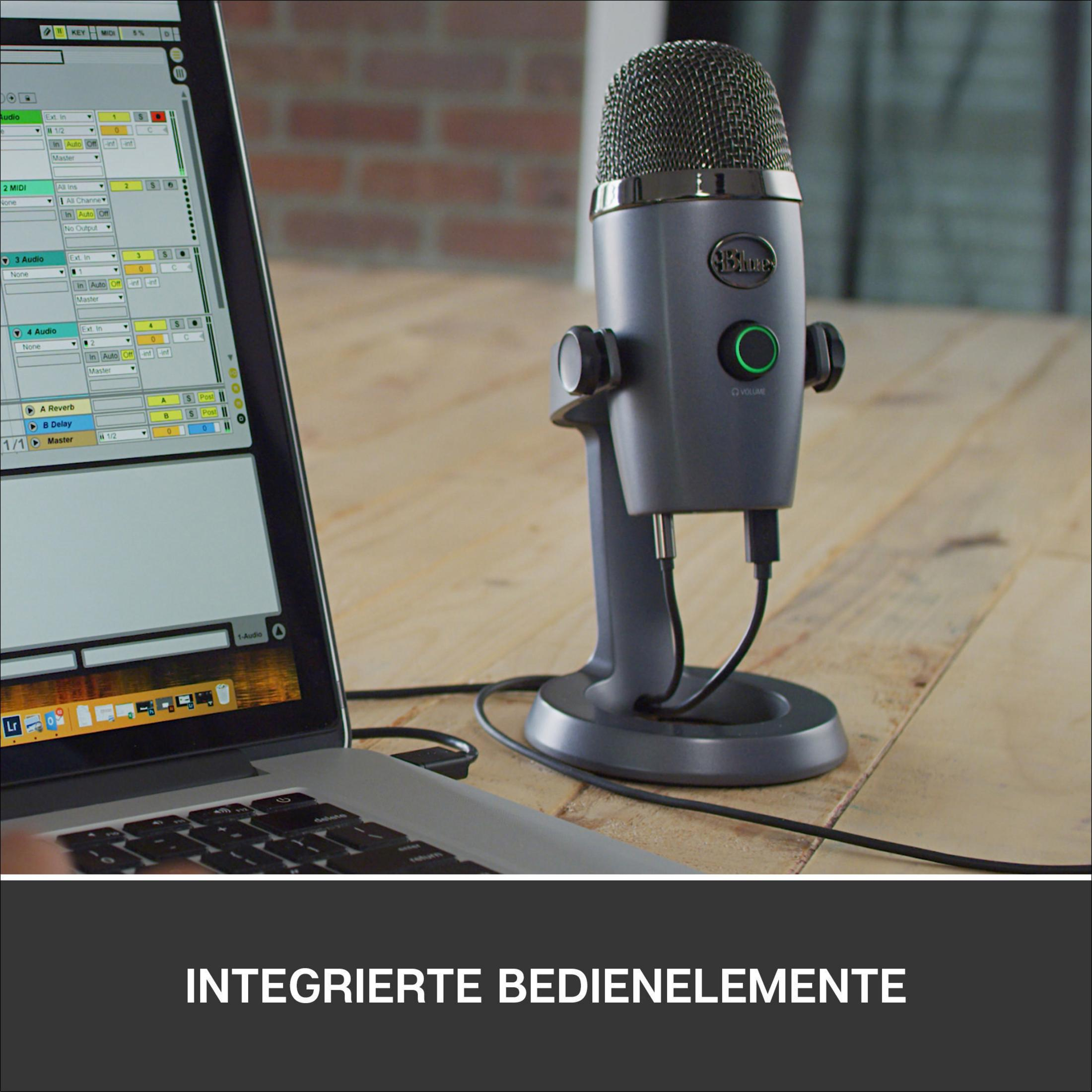 Graues Mikrofon auf einem Ständer. Laptop und Audio-Interface auf einem Holztisch.