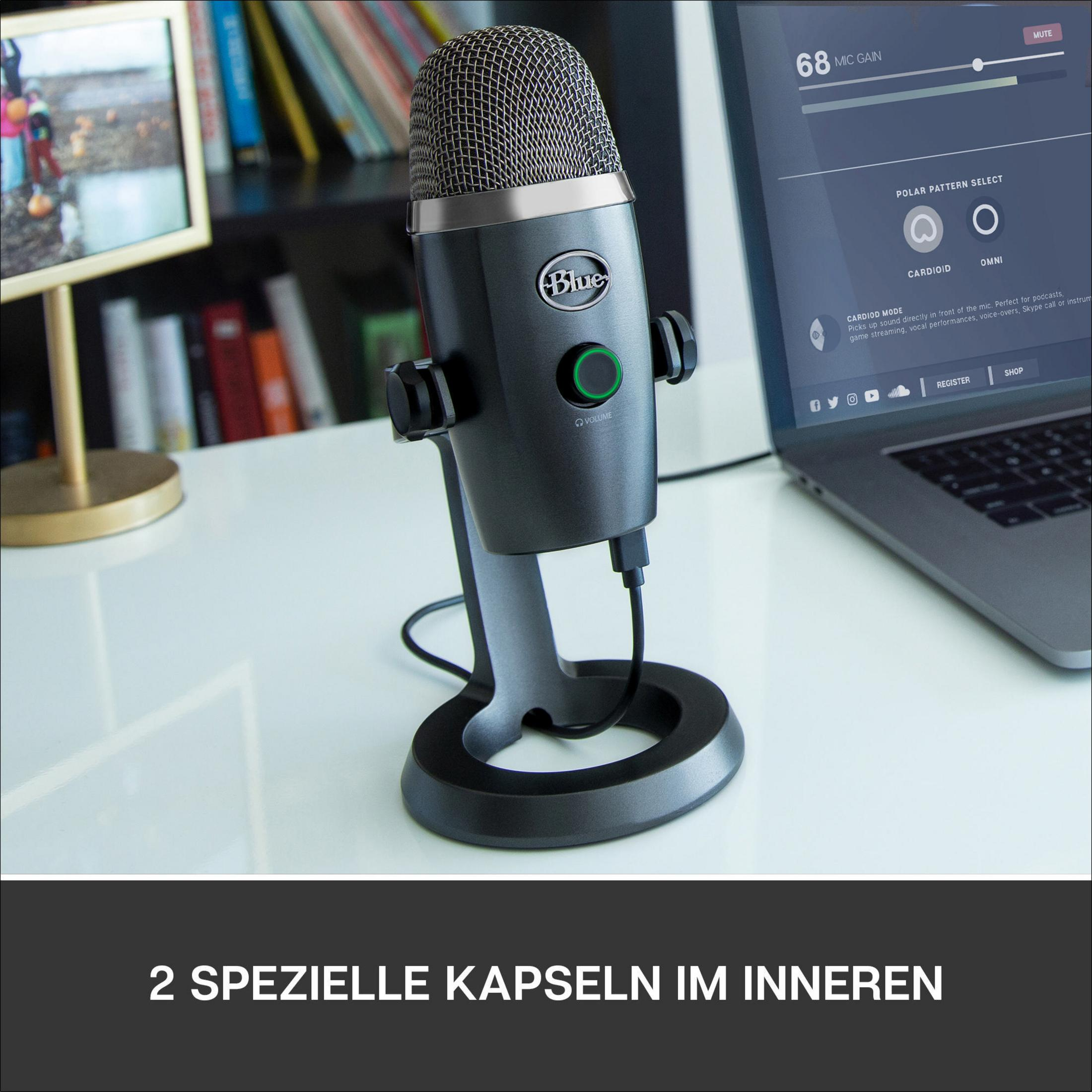 Ein blaues Mikrofon auf einem Ständer, ein Laptop und Bücher stehen auf einem weißen Schreibtisch.
