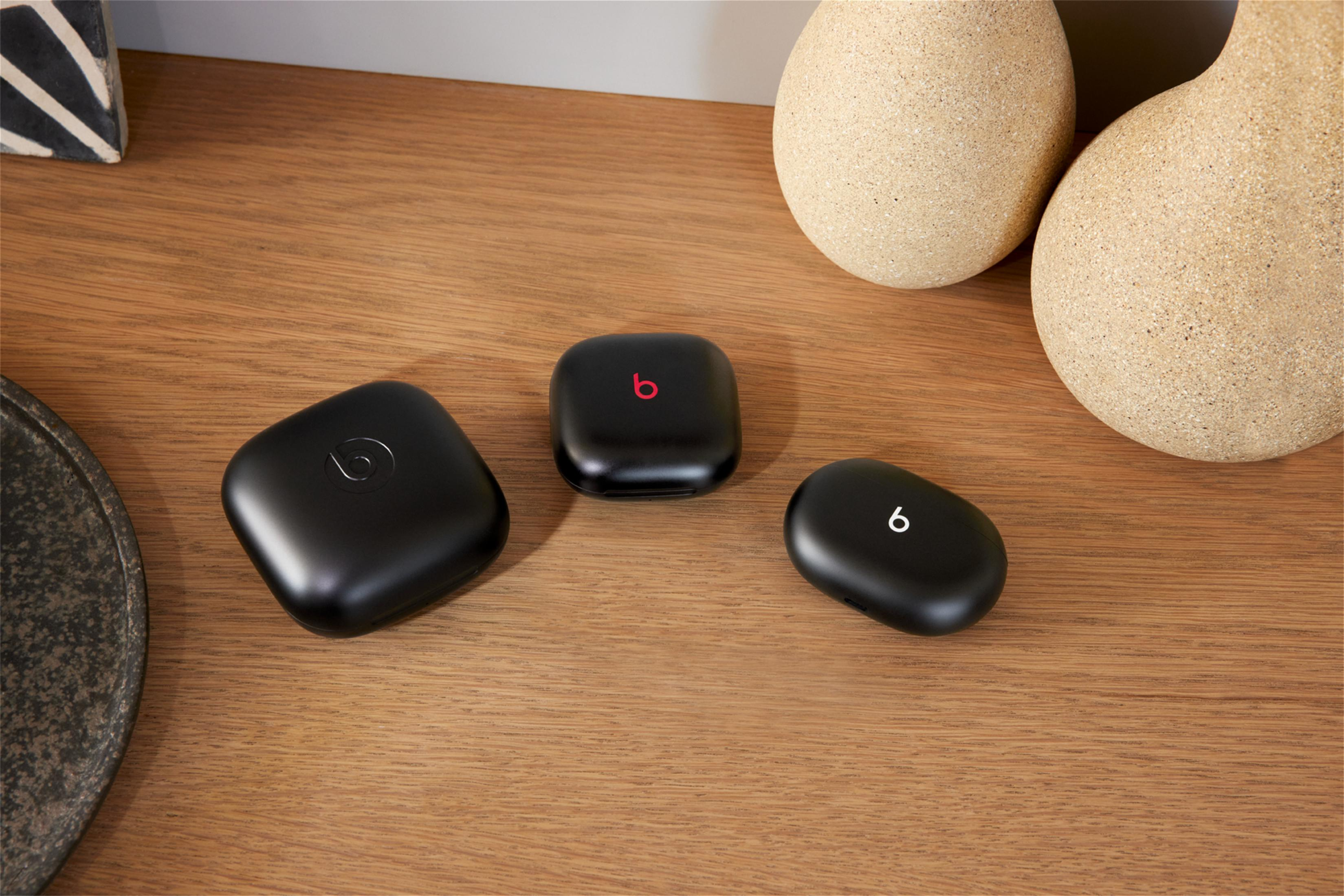 Trzy czarne etui na słuchawki Beats, jedno z czerwonym logo, na drewnianej powierzchni.