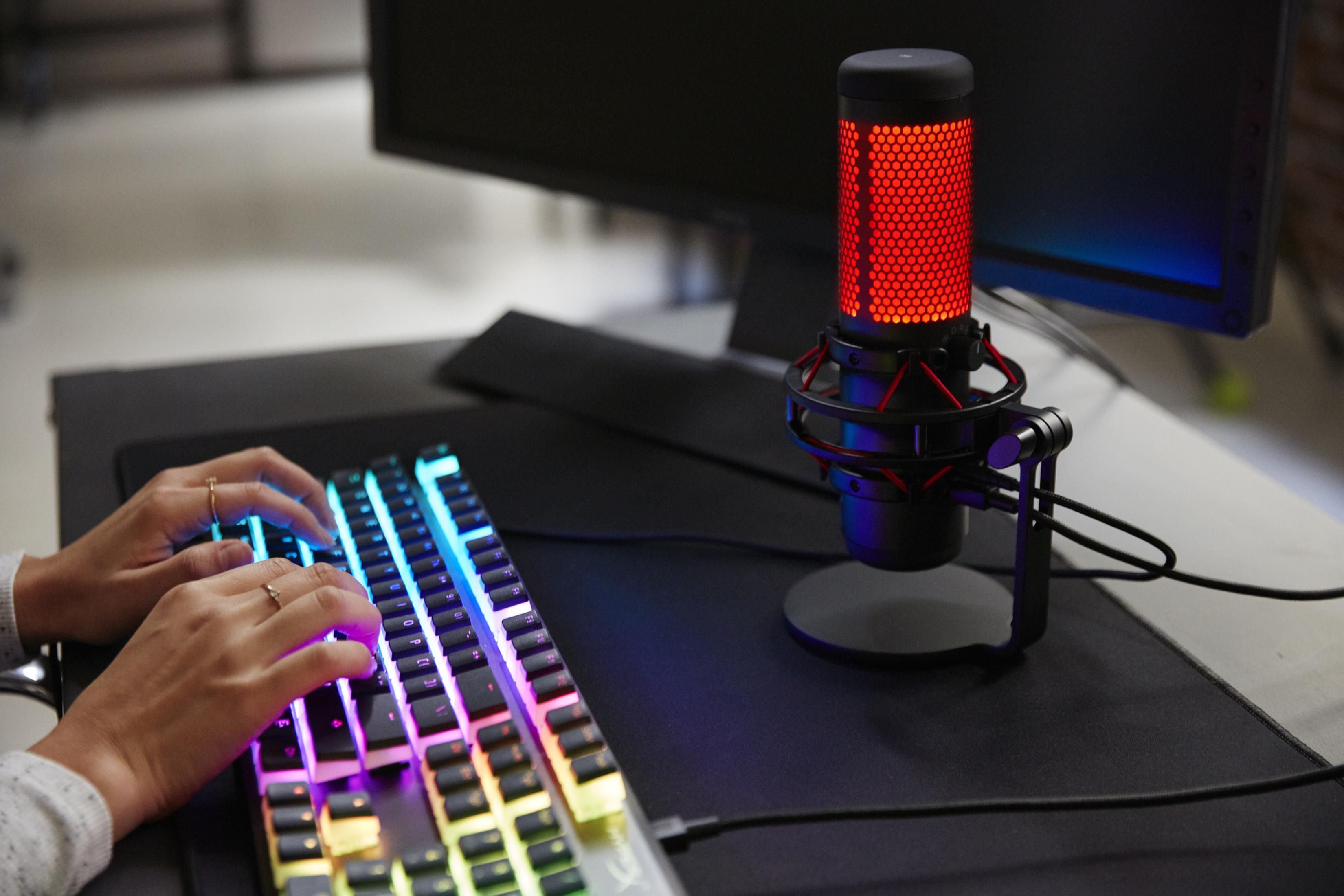Person tippt auf einer hintergrundbeleuchteten Tastatur. Ein rotes Mikrofon steht daneben.