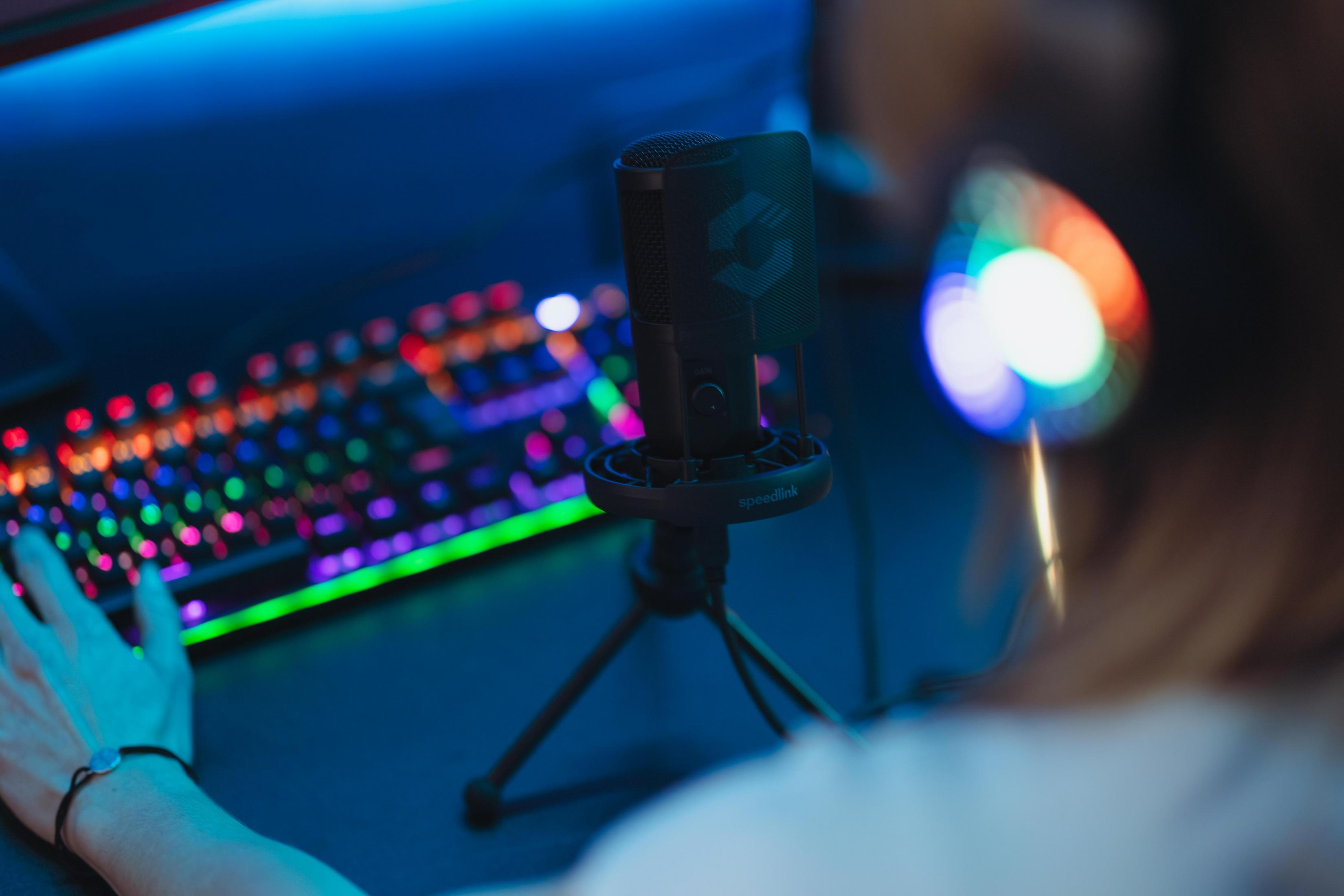 Eine Person benutzt eine Tastatur und ein Mikrofon mit einem farbenfrohen Gaming-Setup.