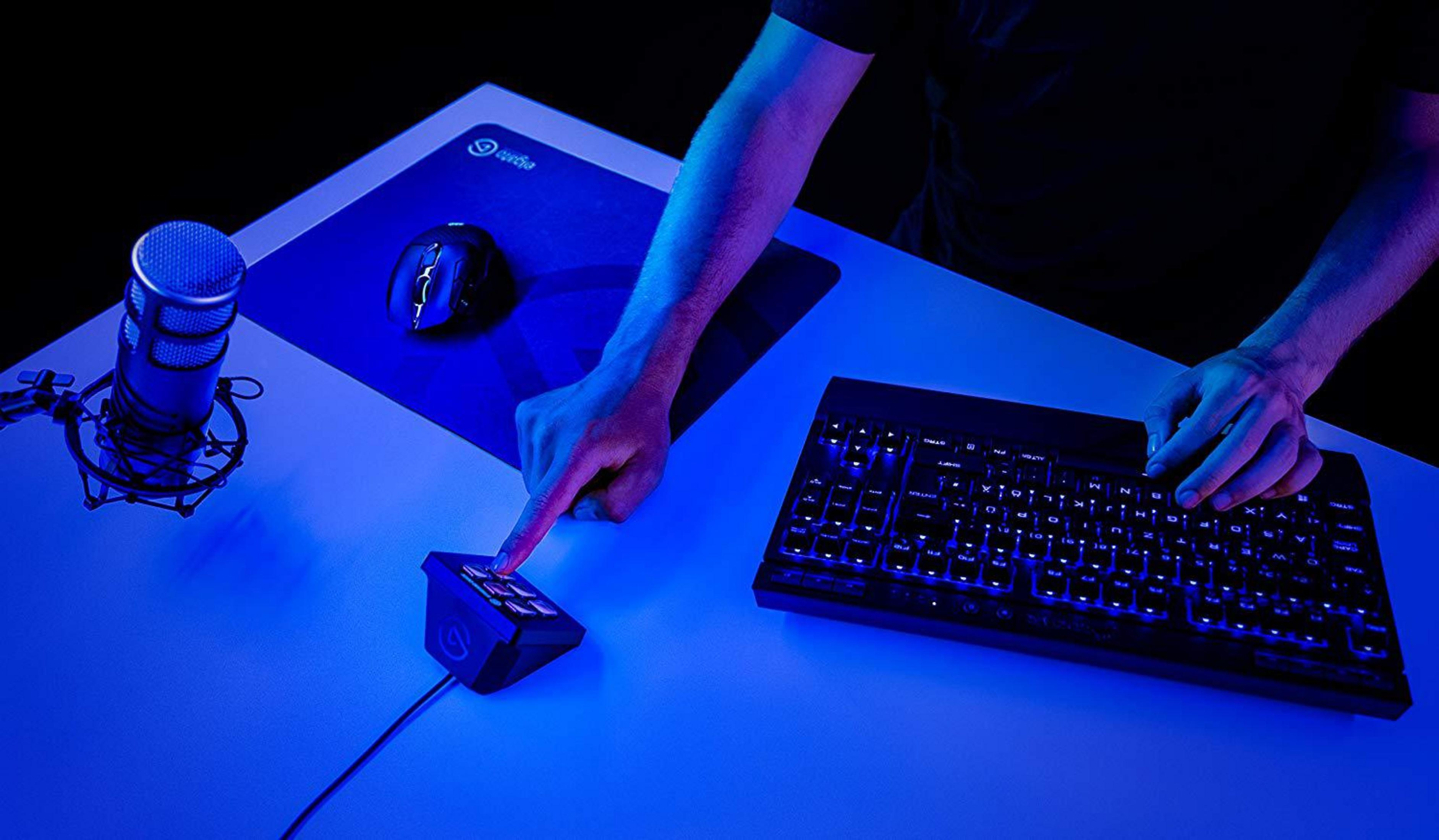 Ręka osoby dotyka przycisku na klawiaturze, z myszą i mikrofonem na biurku.