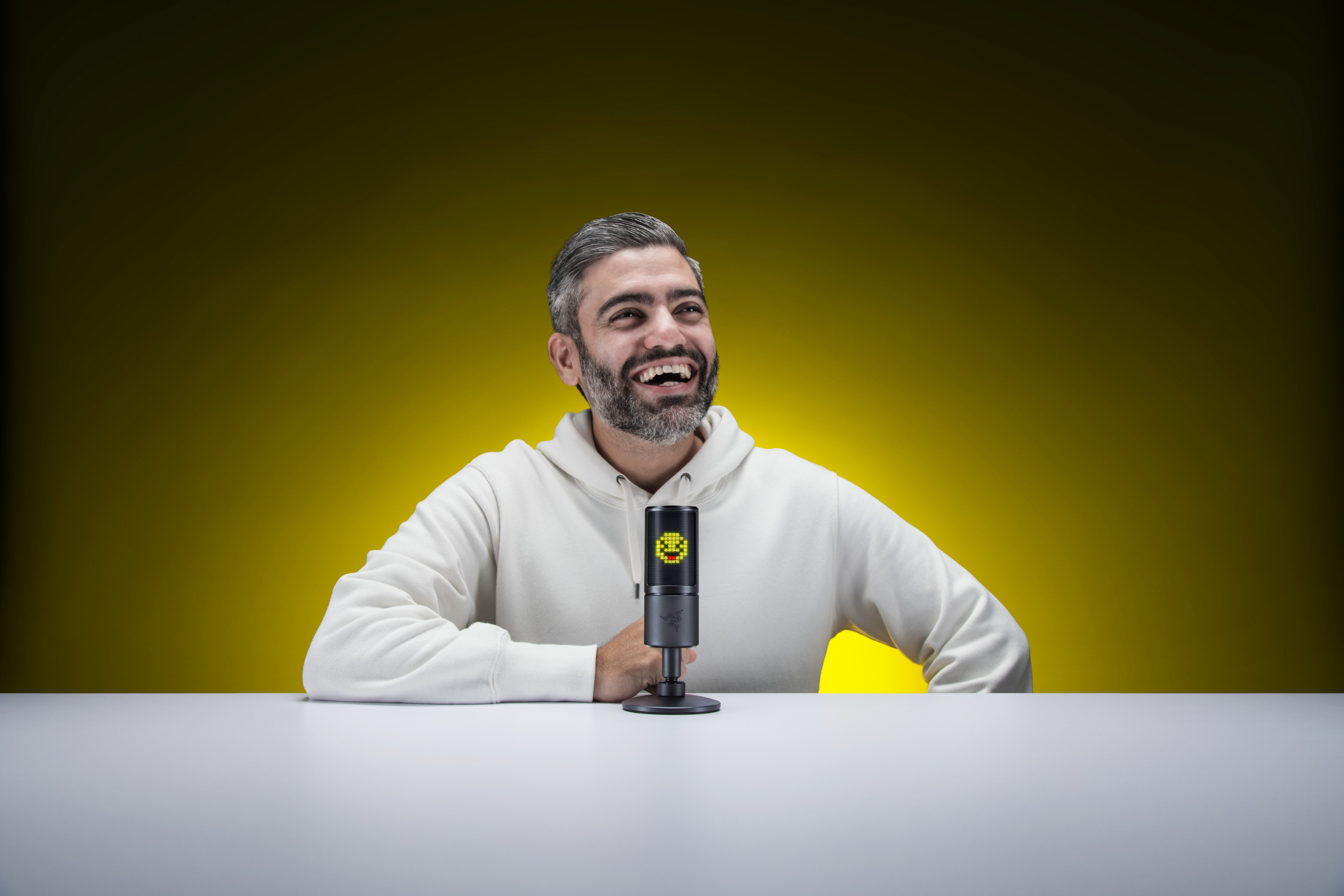 Mężczyzna śmieje się, siedząc przy stole, z mikrofonem.