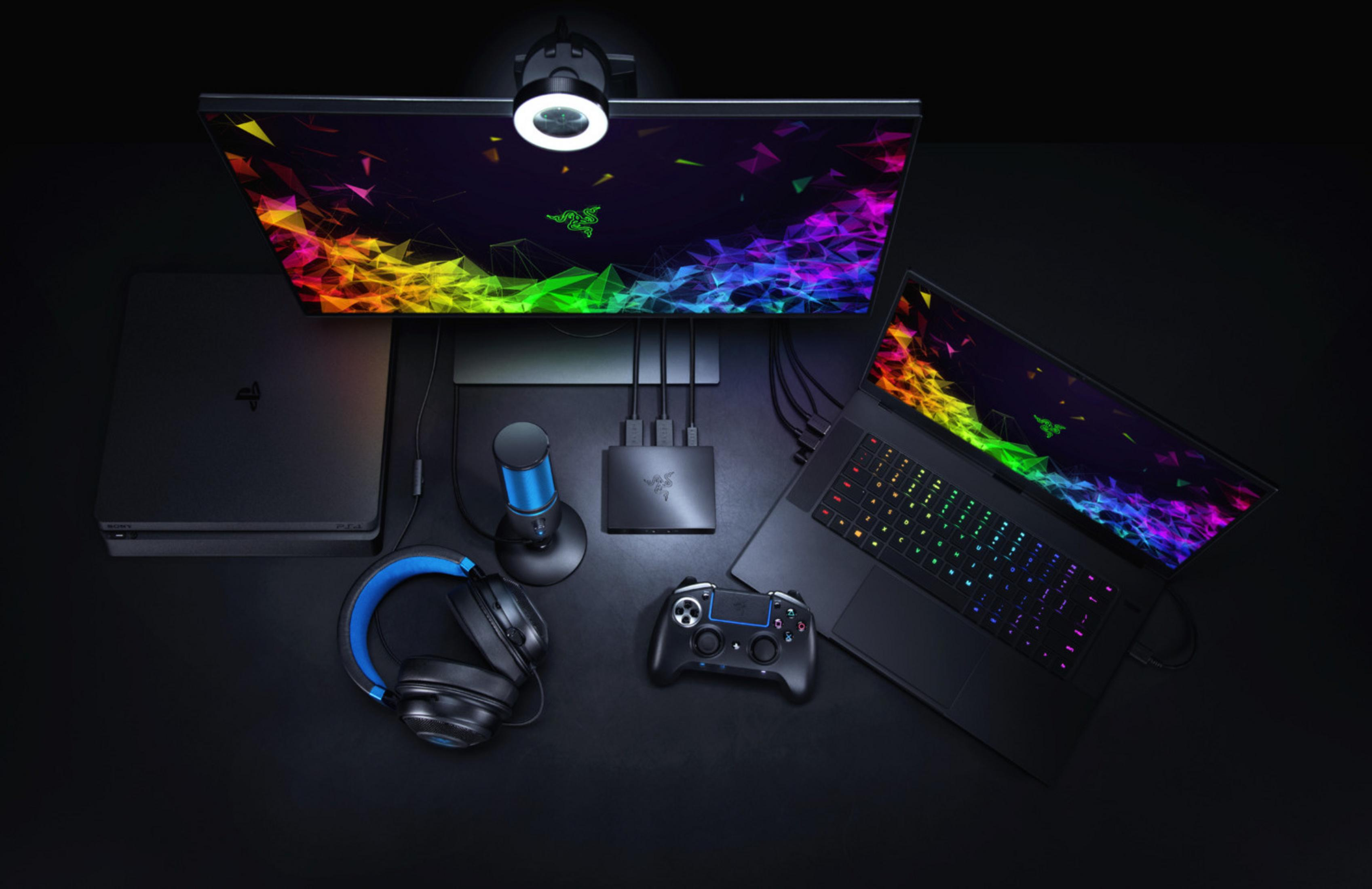 Configuración de juegos: monitor, portátil, auriculares, mando, micrófono y un concentrador en un escritorio negro.