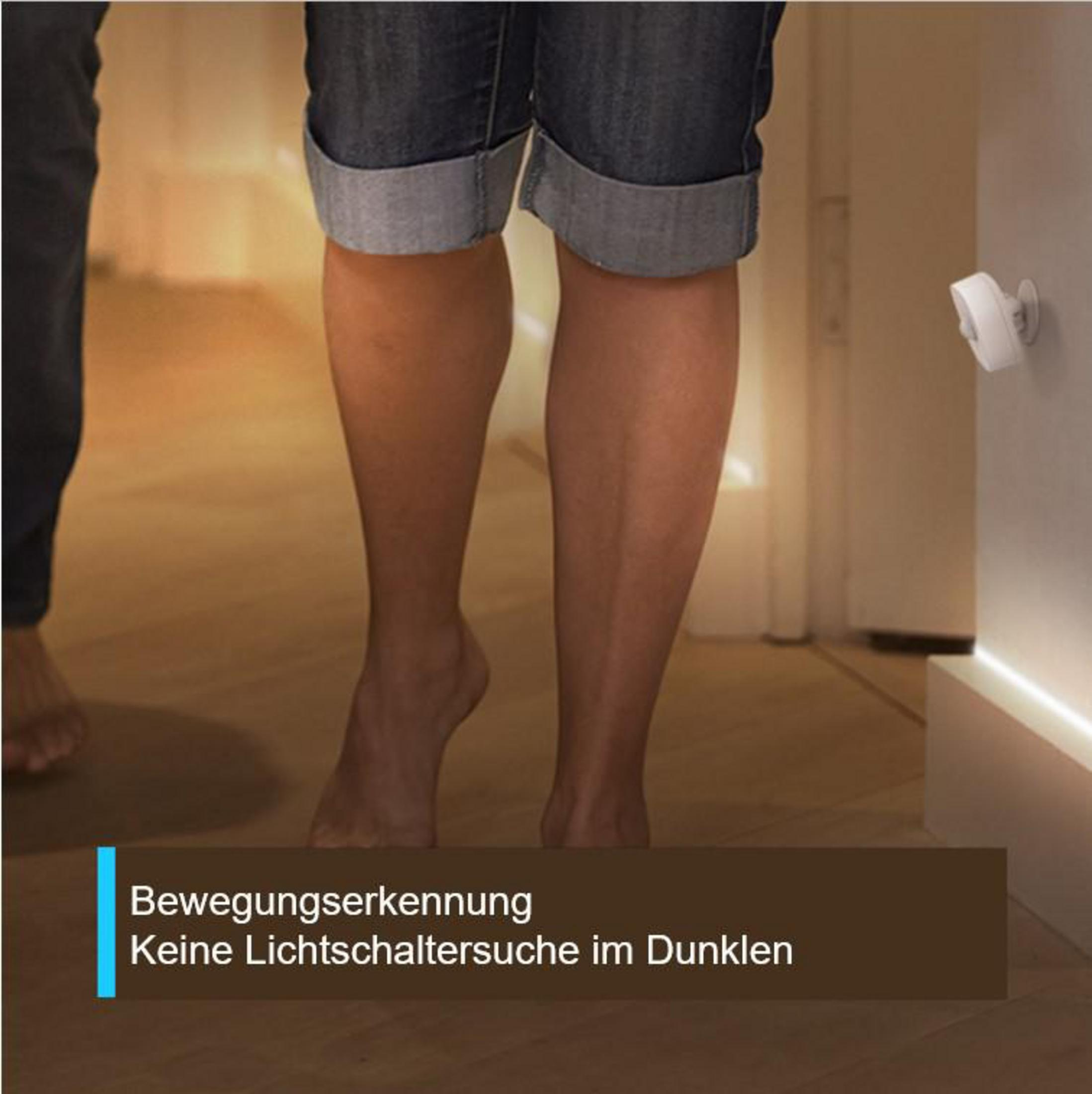 Beine einer Person, die durch einen Flur geht. Eine Überwachungskamera ist an der Wand montiert.
