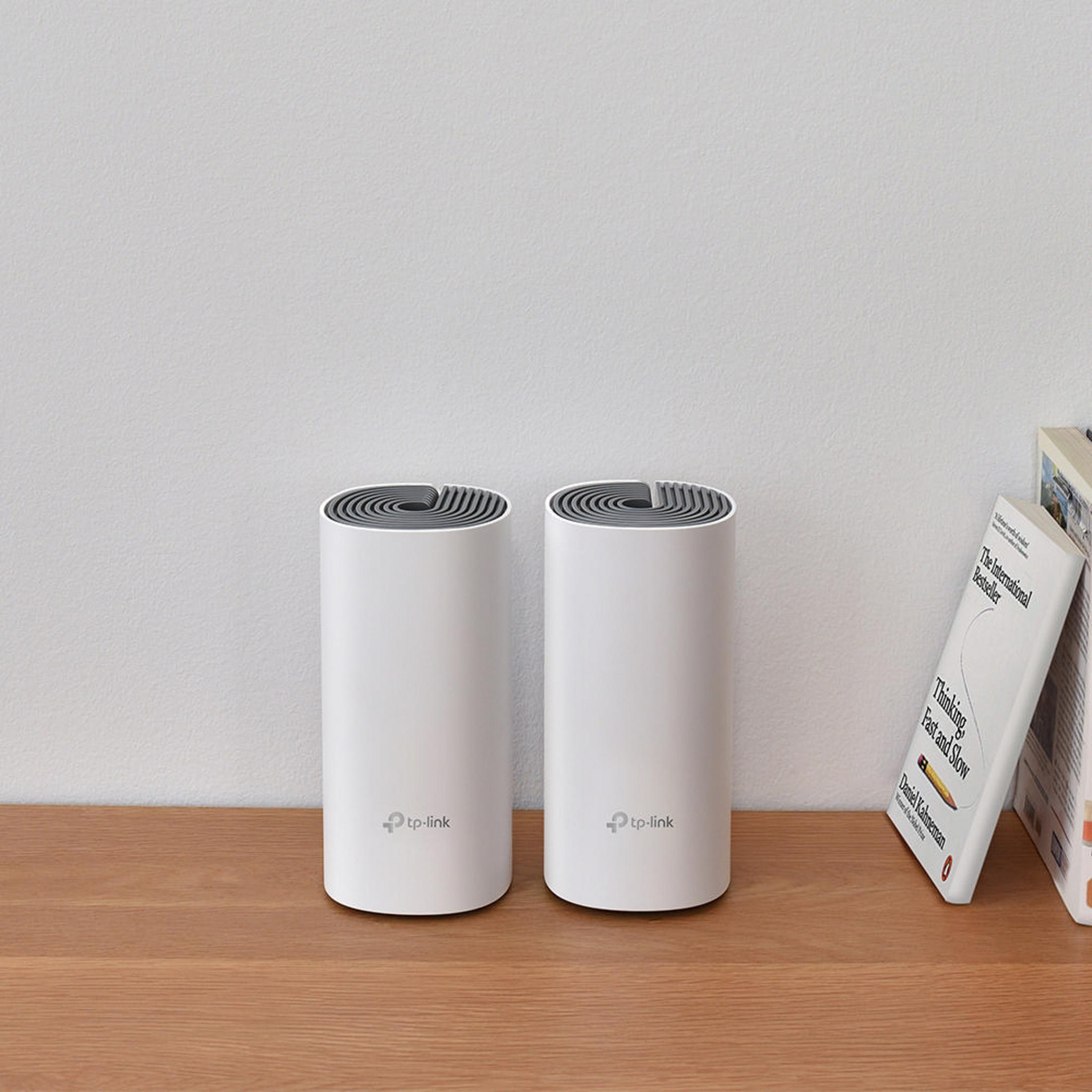 Twee witte cilindervormige routers op een houten tafel, met witte achtergrond.