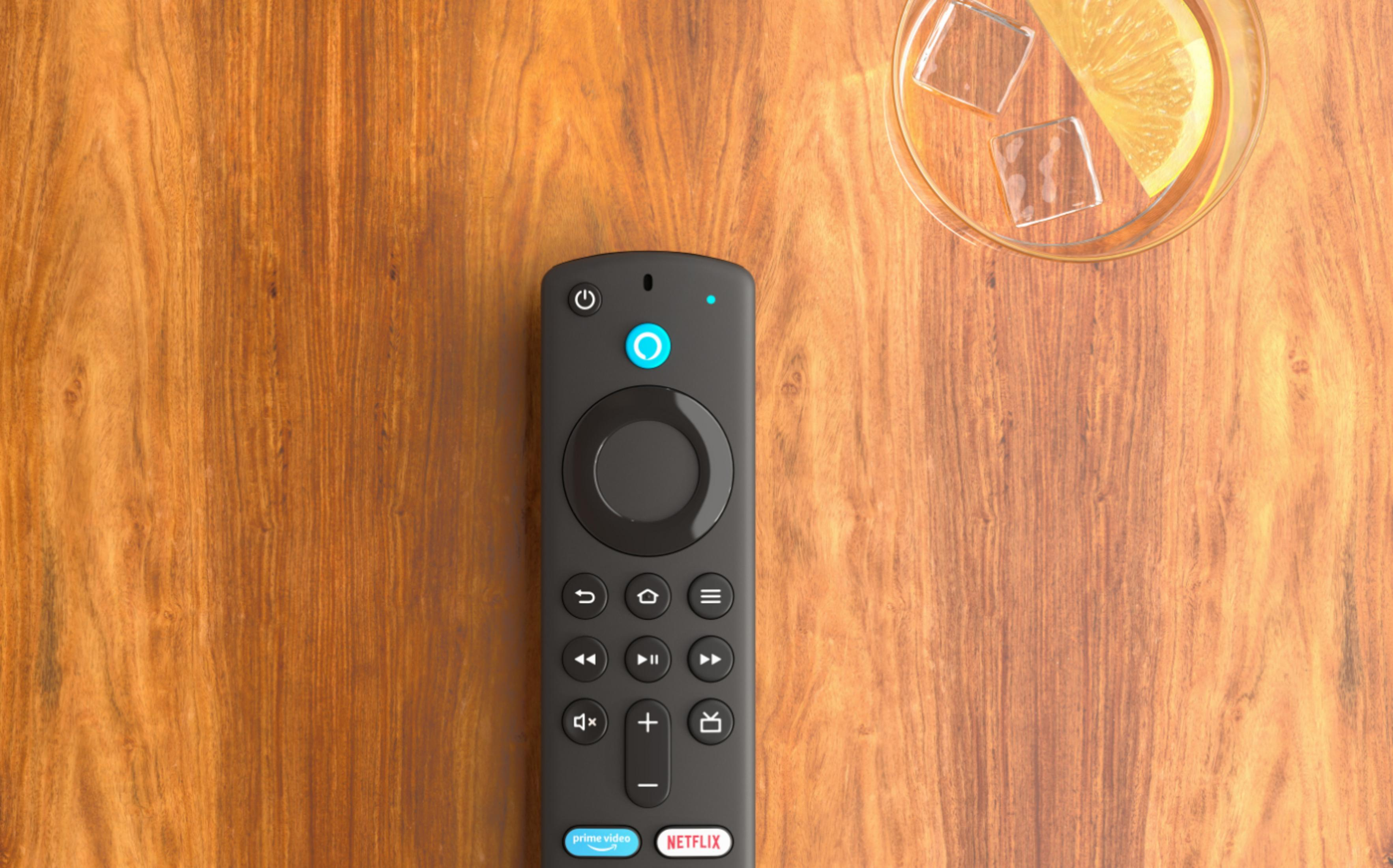 Schwarze Fire TV-Fernbedienung und ein Glas Getränk mit Eis und Zitrone auf Holztisch.