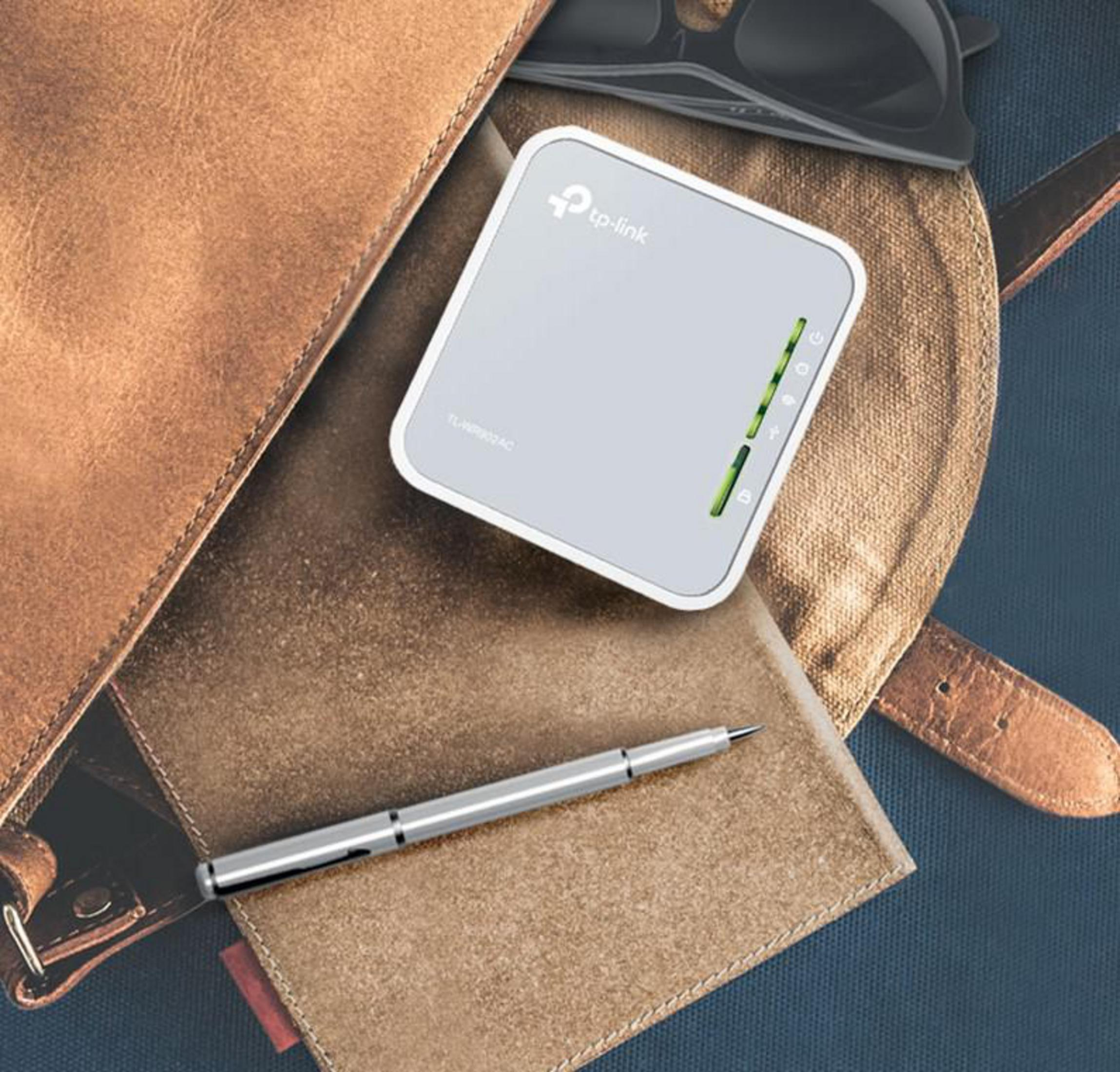 Mały biały router, okulary i długopis leżą na skórzanej torbie.