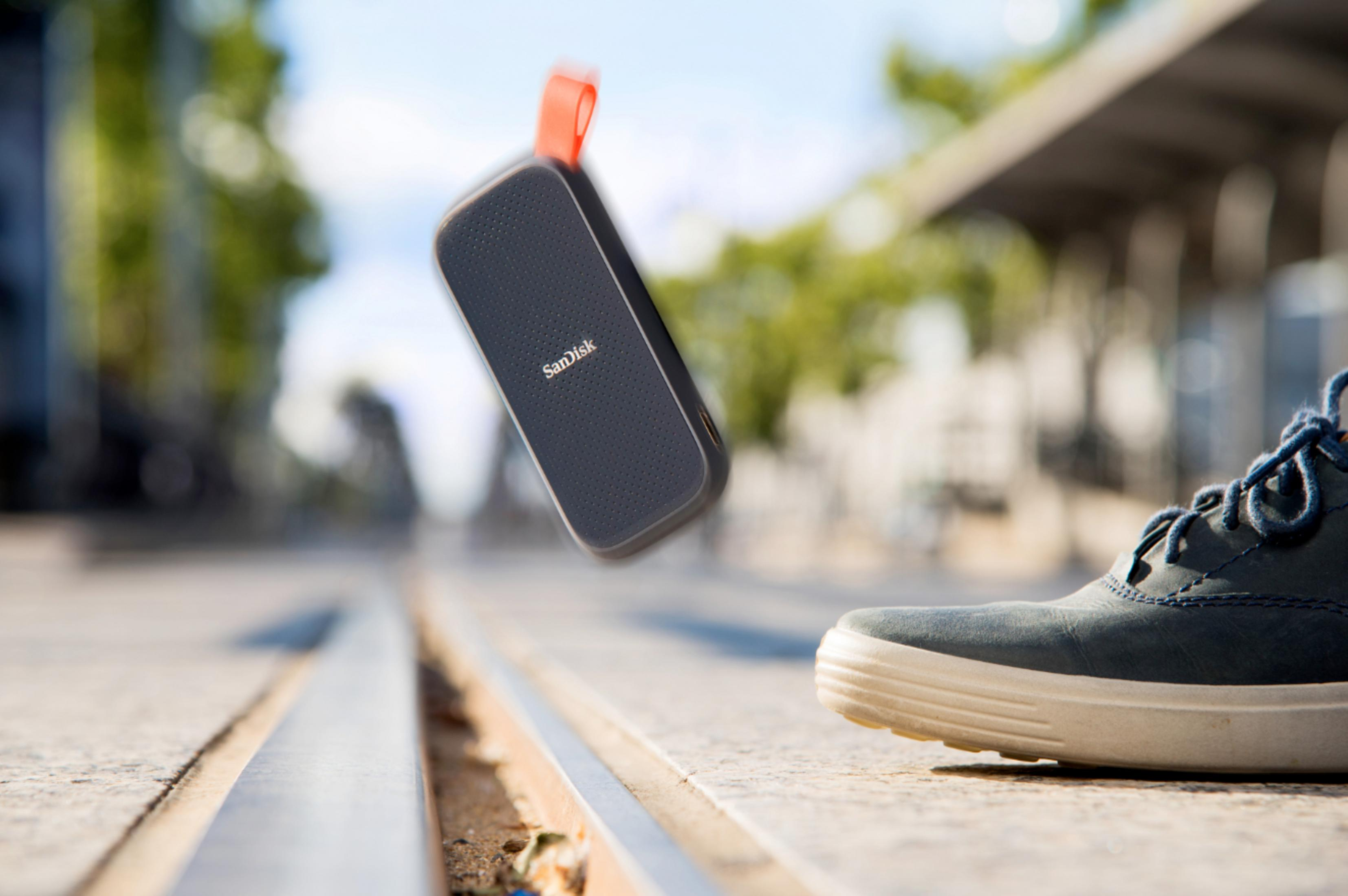 Czarny i szary zewnętrzny dysk twardy SanDisk spada w kierunku stopy na ulicy miejskiej.