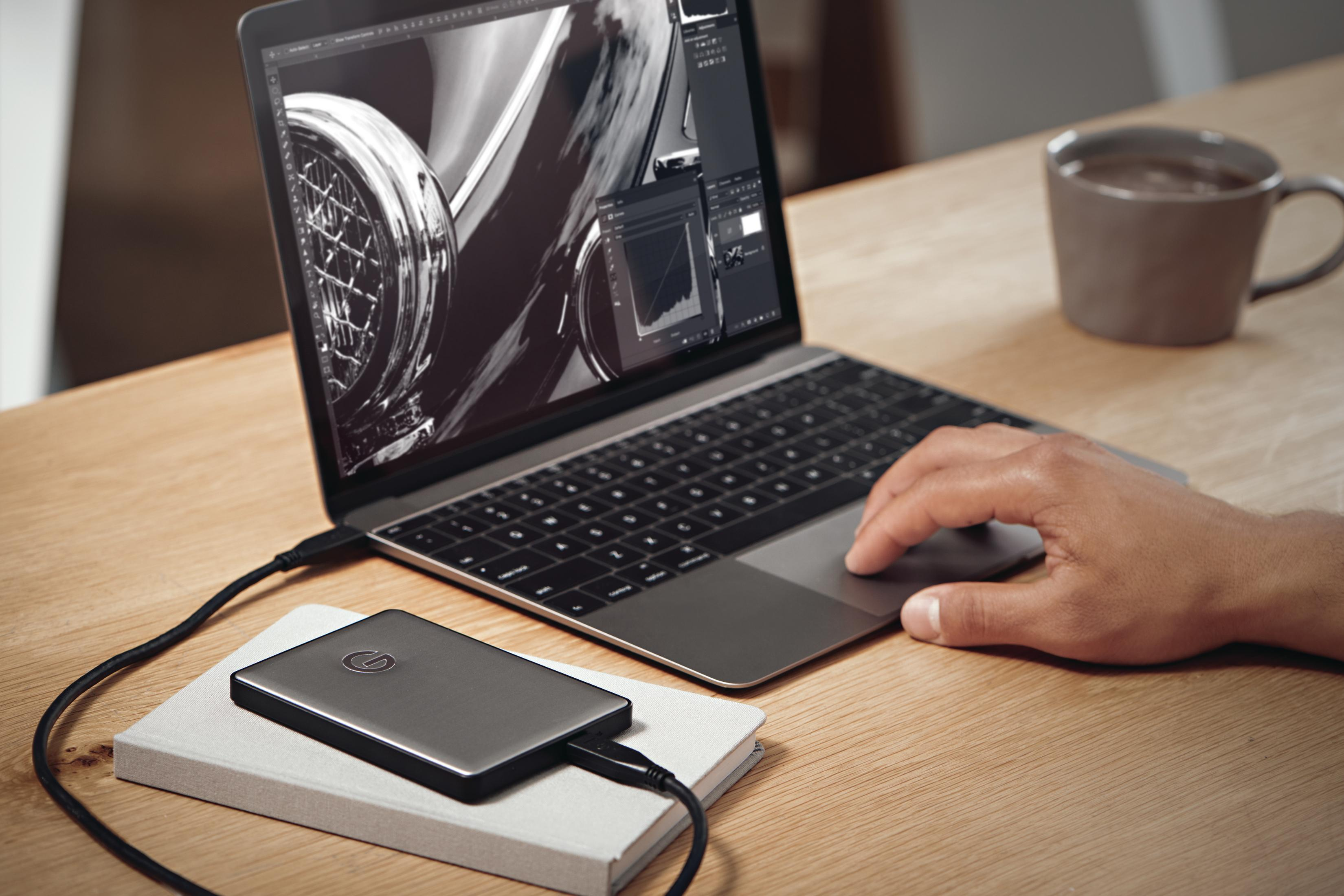Laptop offen auf Holztisch, an externe Festplatte angeschlossen. Eine Tasse Kaffee steht daneben.