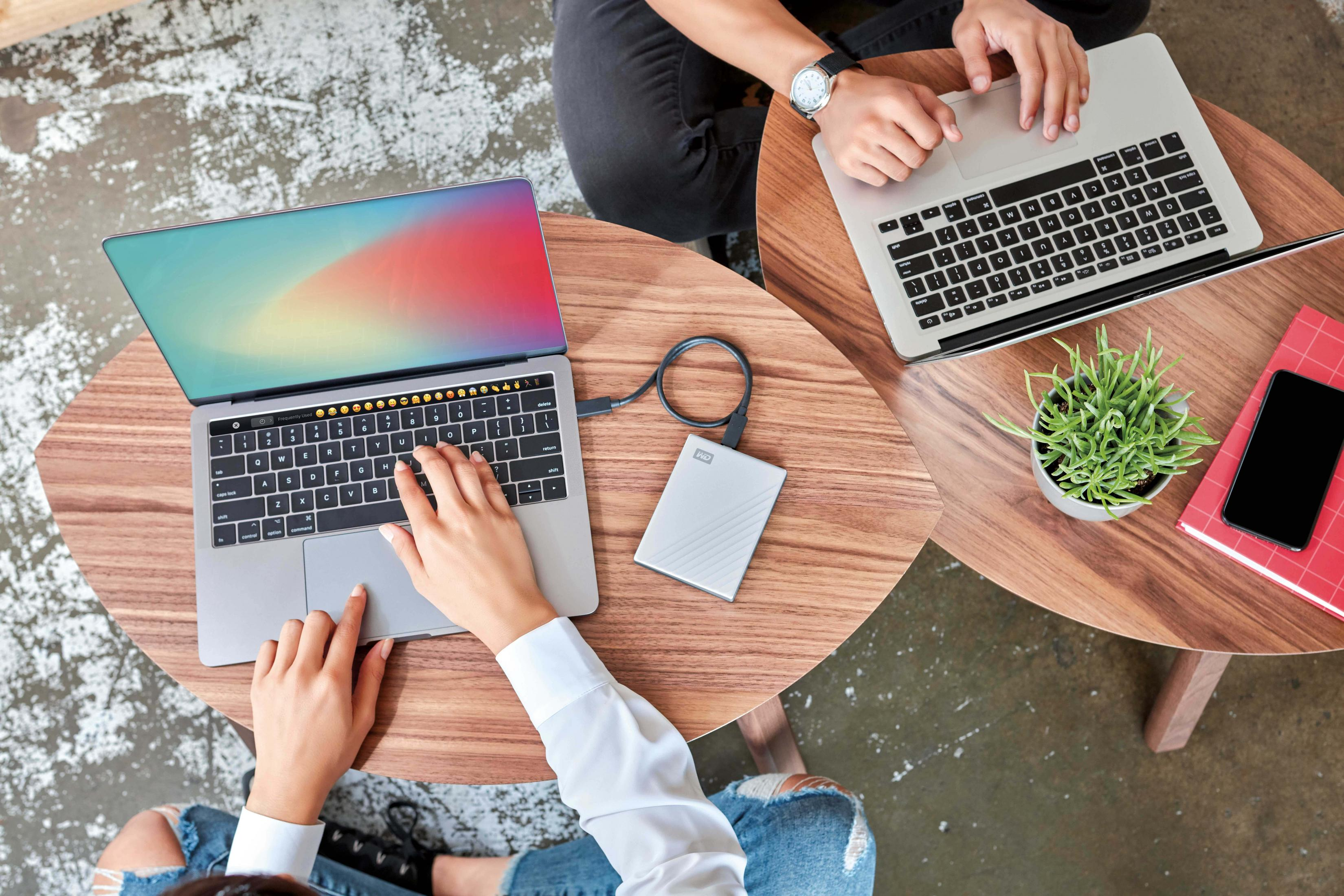 Dwie osoby używają laptopów i dysku twardego na stole, widok z góry.