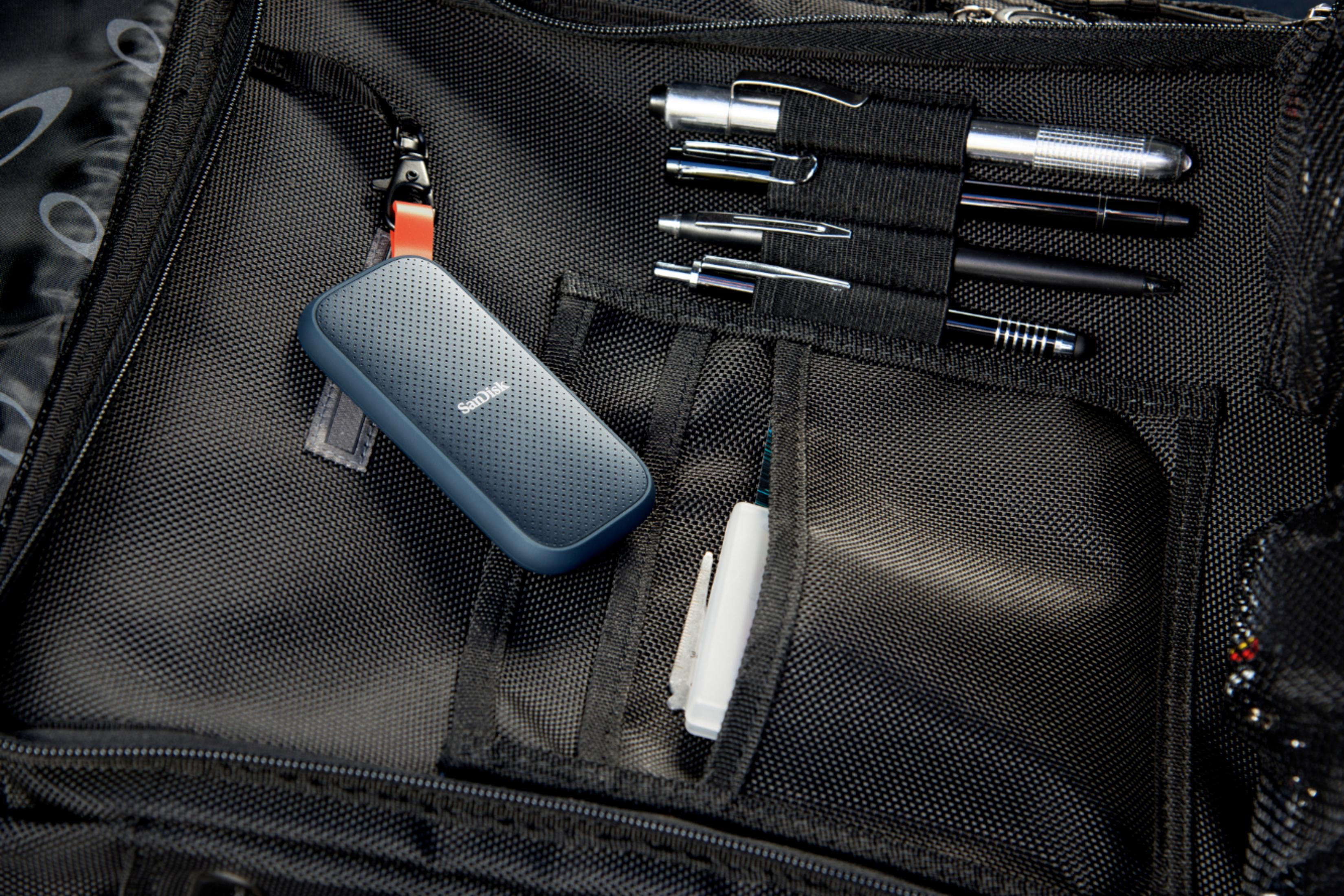 Niebieski przenośny dysk SSD SanDisk w czarnej torbie z długopisami i piórnikiem.