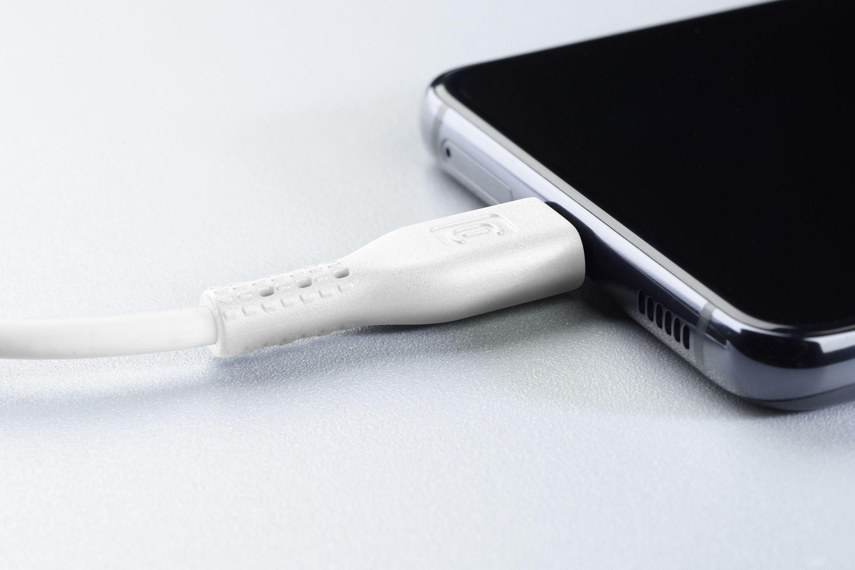 Cavo di ricarica bianco collegato a uno smartphone nero, su una superficie grigia.