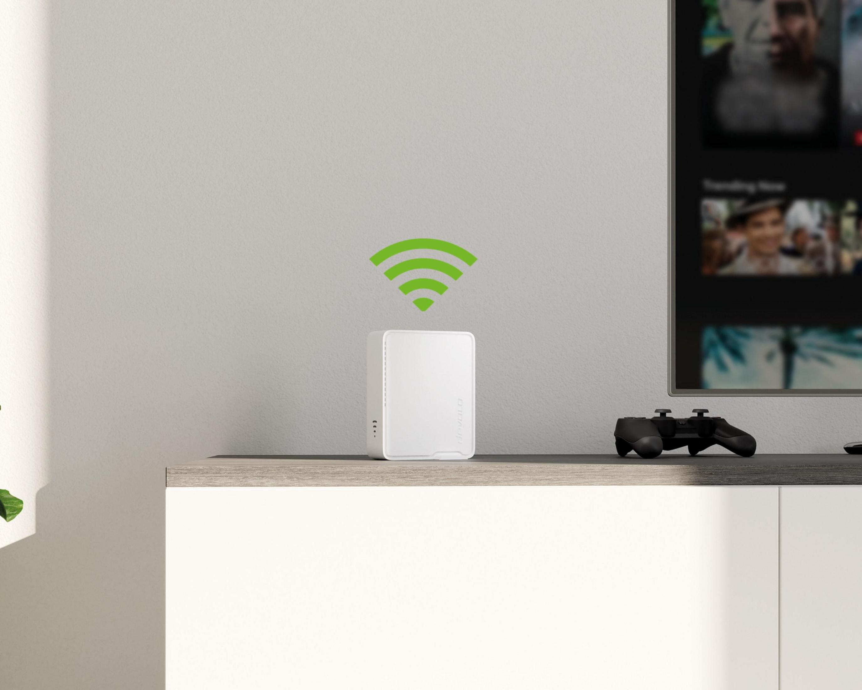 Biały router z symbolem wifi na półce obok telewizora i kontrolera do gier.