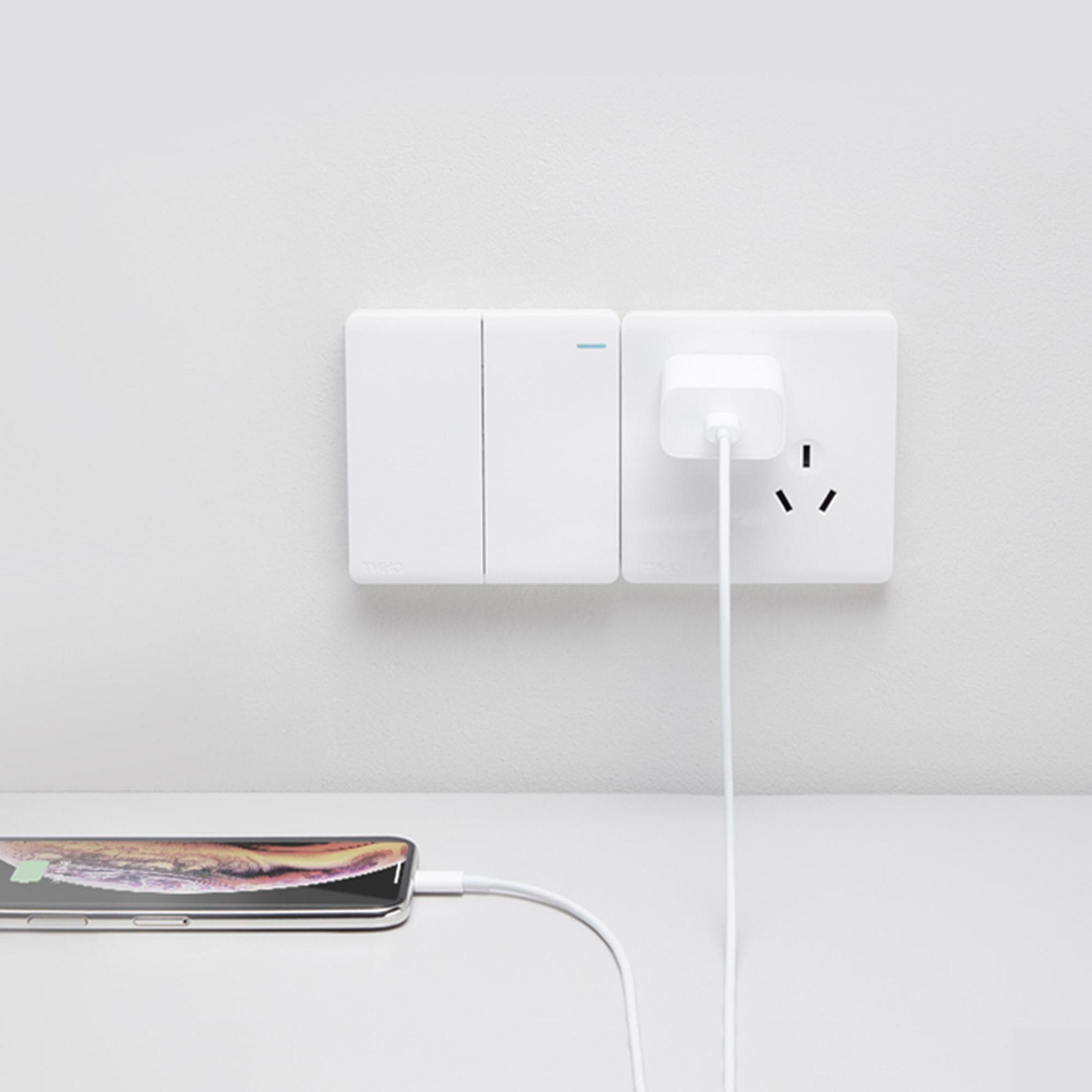 Weiße Wand mit Lichtschaltern und Steckdose. Telefon wird geladen.