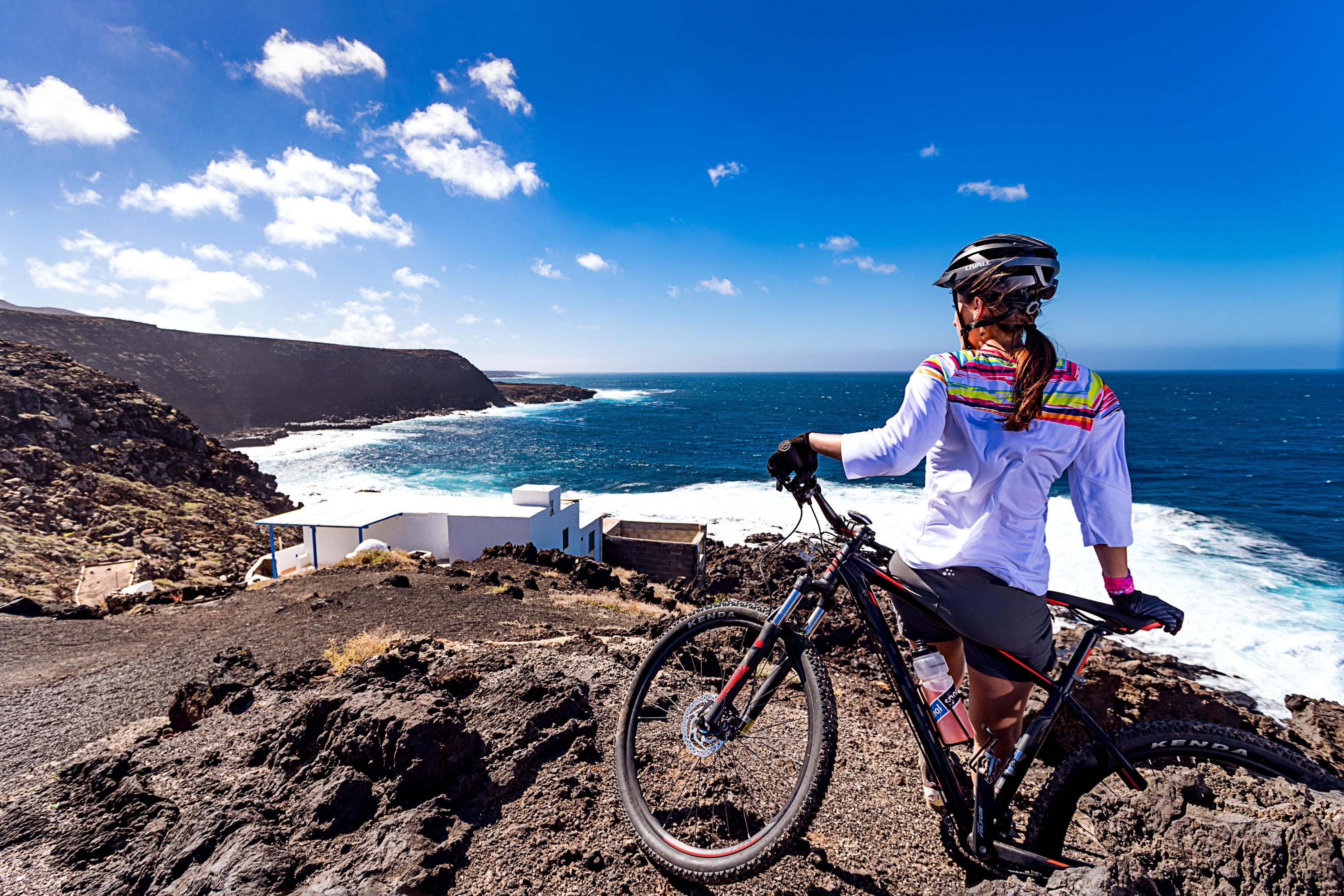 Frau auf Mountainbike, blickt am sonnigen Tag auf das Meer.