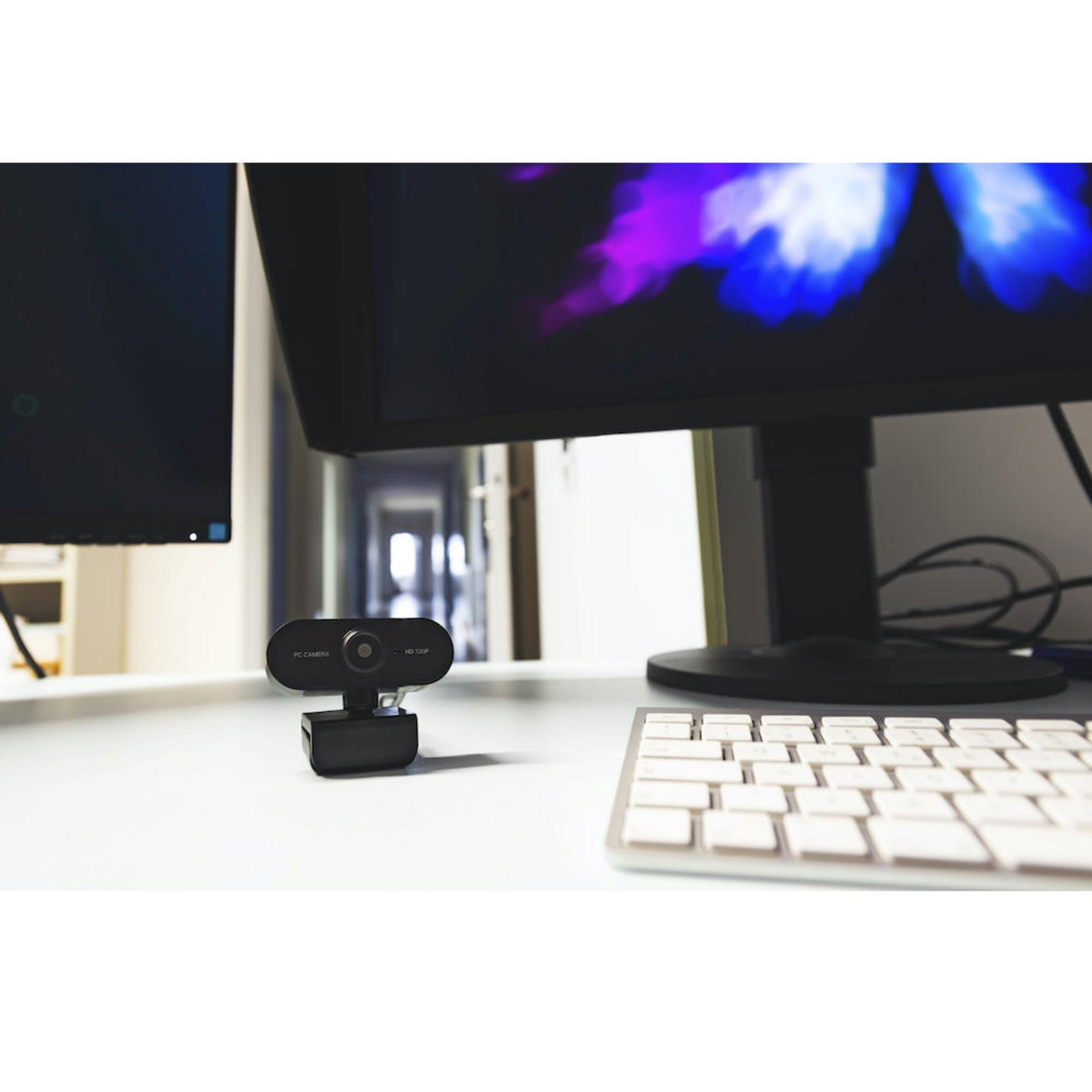 Kamera internetowa na biurku, z monitorem, klawiaturą i tłem z korytarzem.