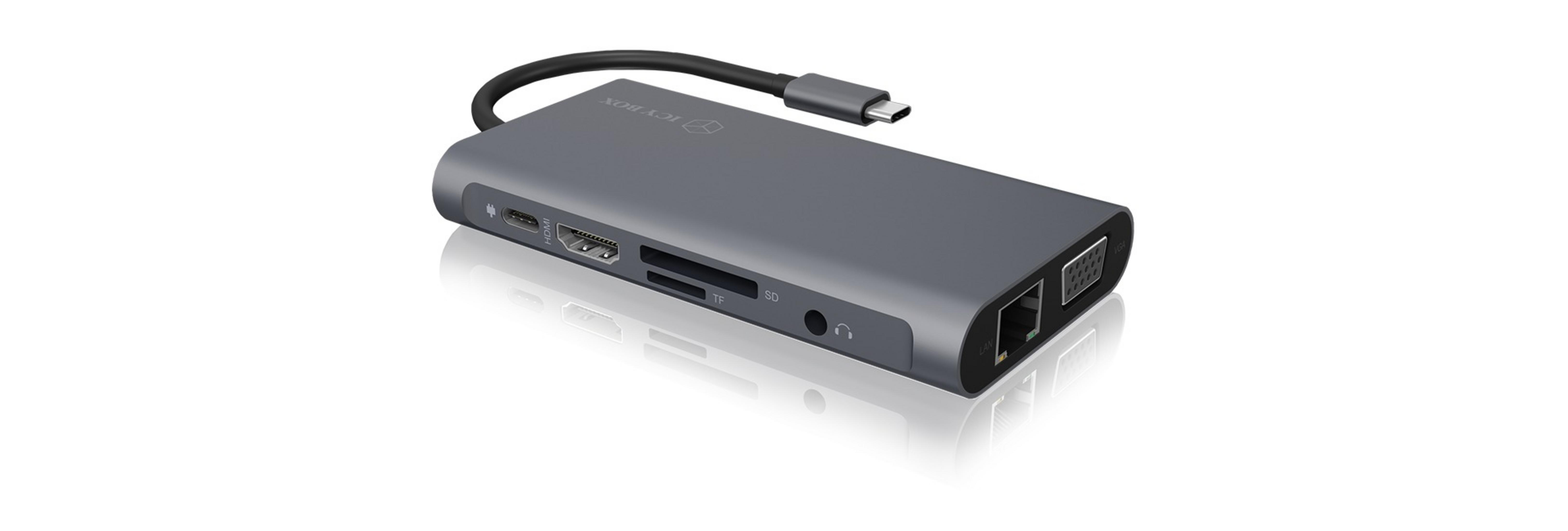 Un hub USB-C grigio con più porte, tra cui HDMI, USB e slot per schede SD, su una superficie bianca.