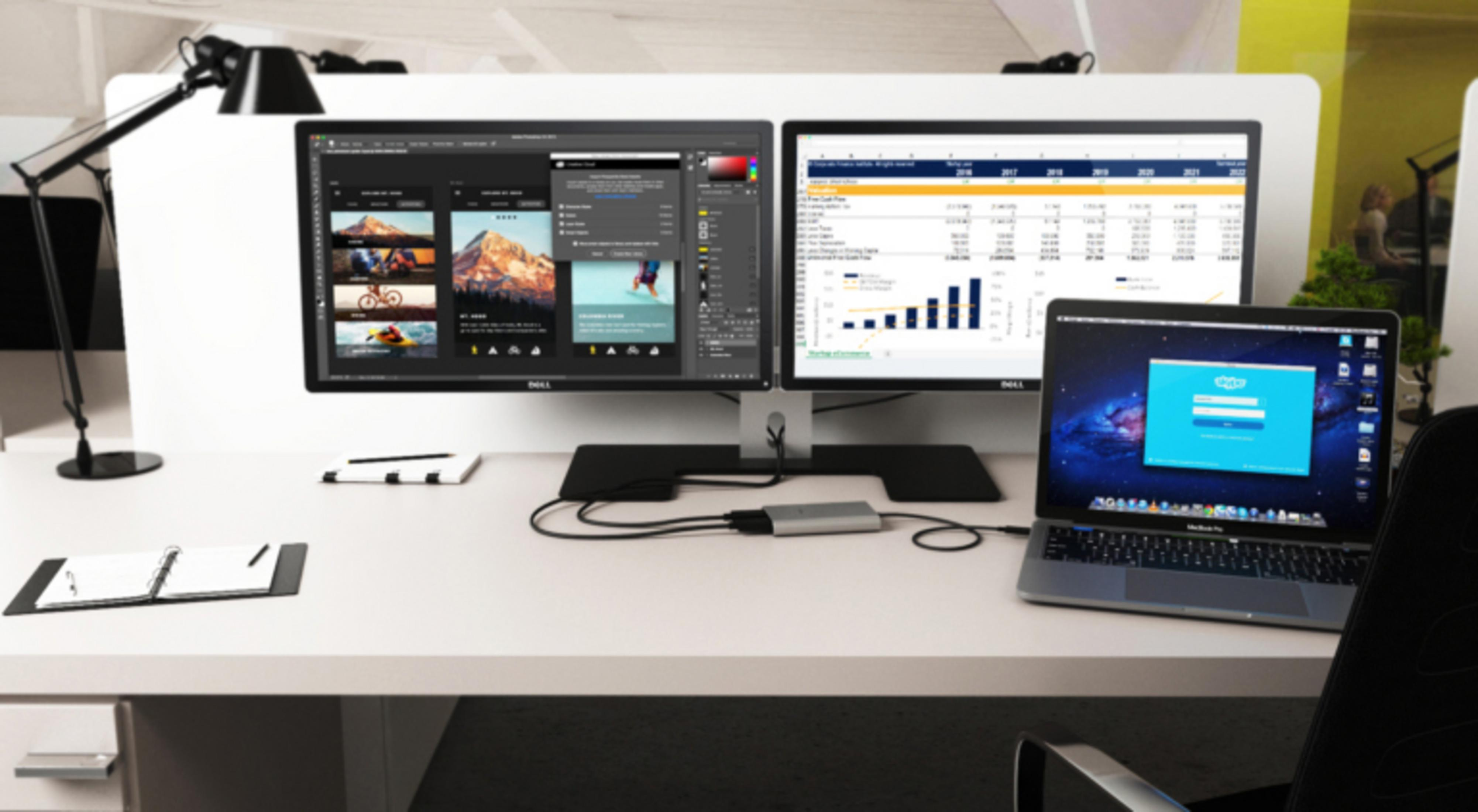 Un escritorio blanco con dos monitores, una computadora portátil y suministros de oficina. La computadora portátil muestra una pantalla de inicio de sesión de Skype.