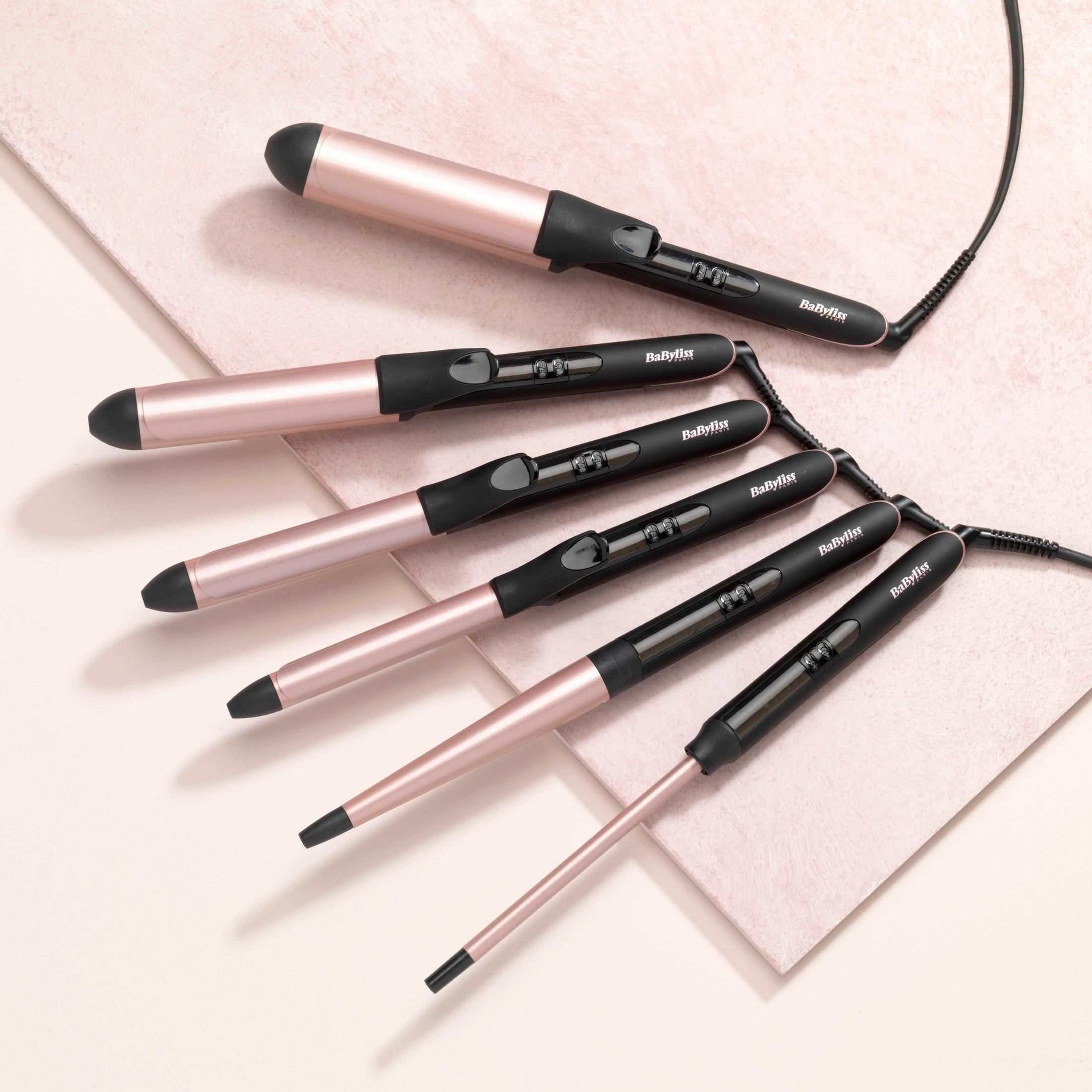 Zestaw lokówek o różnych rozmiarach. Czarno-różowo-złota kolorystyka. Białe tło.