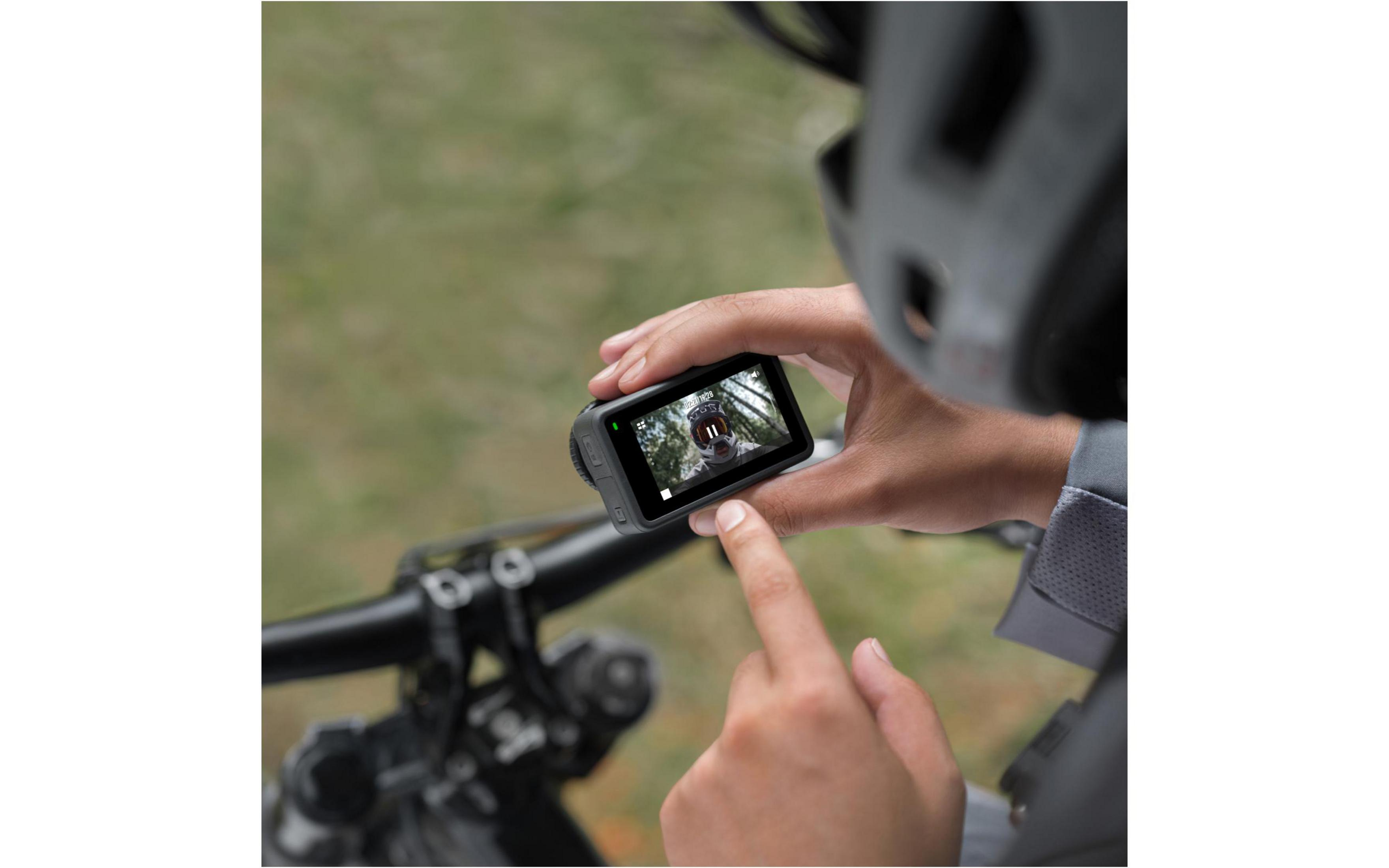 Osoba trzymająca małą kamerę sportową, pokazującą scenę leśną na ekranie.