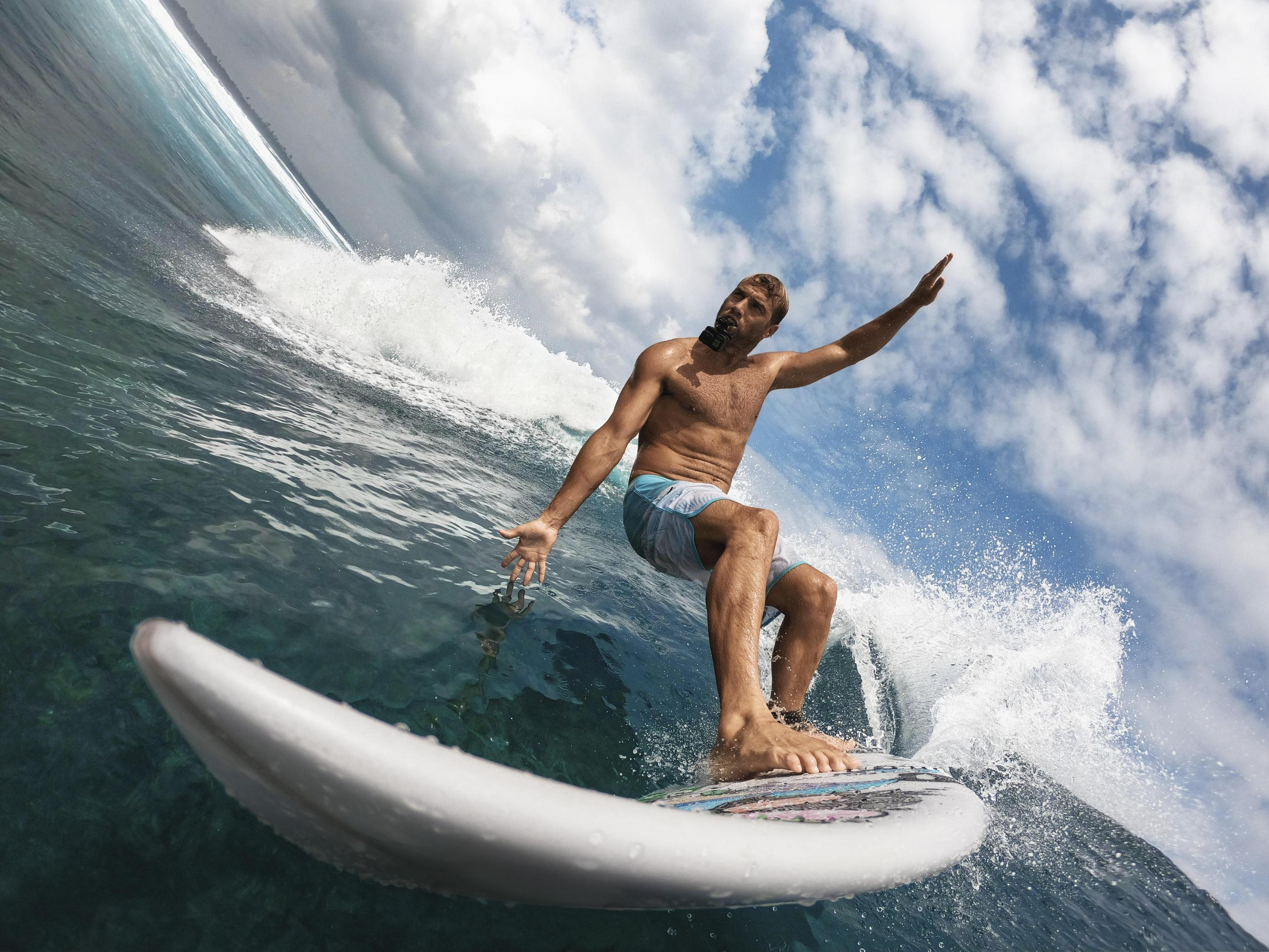 Ein Surfer reitet eine Welle, mit ausgestreckten Armen, mit einer Kamera im Mund.