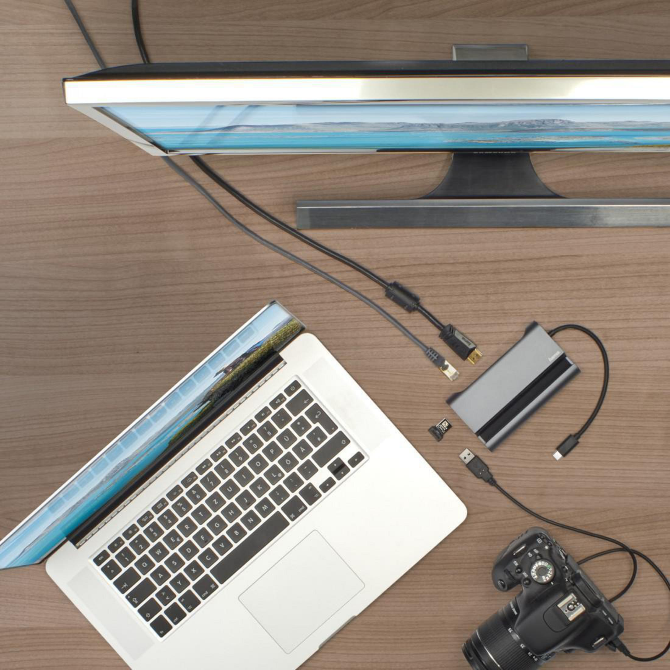Laptop, monitor, cavi e fotocamera su una scrivania di legno. È presente anche un hub.