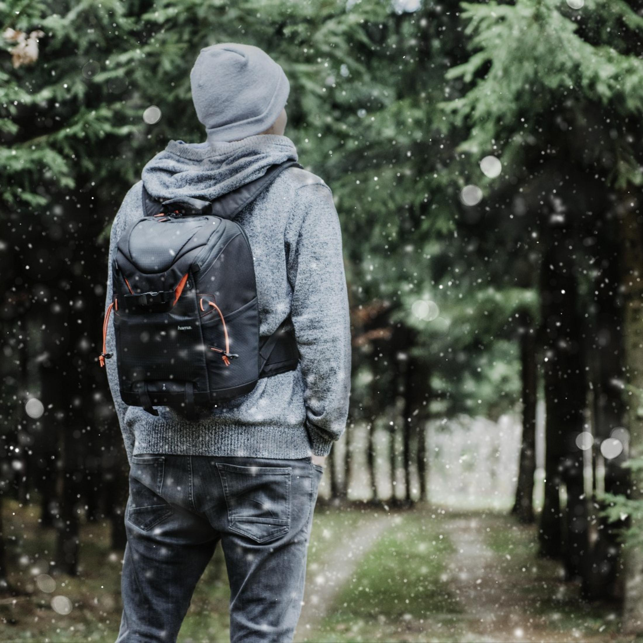 Ein Mann mit grauem Kapuzenpullover und Rucksack geht in einen schneebedeckten Wald.